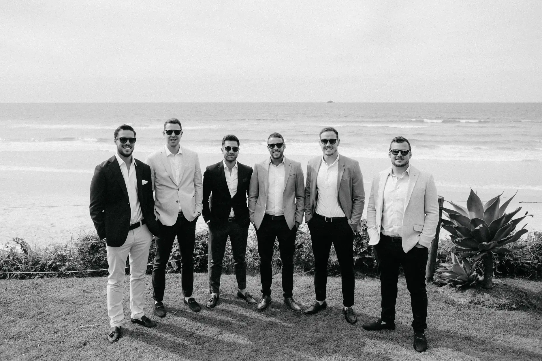 The groomsmen lined up in front of the dunes, black and white, Belongil