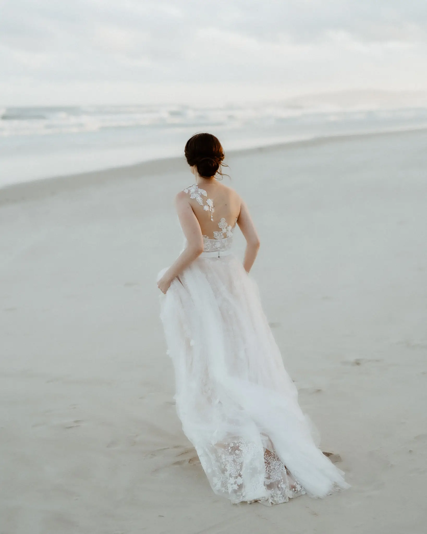 Bride walking alone up the beach, dress trailing