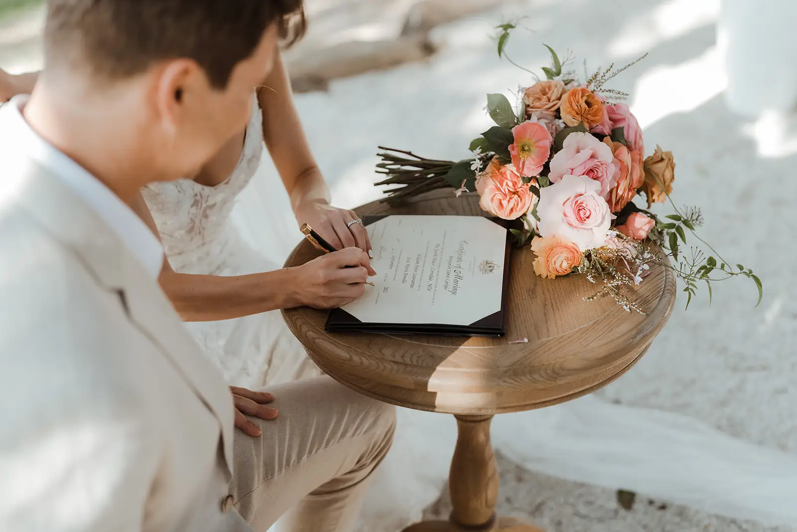 Signing the certificate at a small round timber table beside the bouquet, EarthHouse