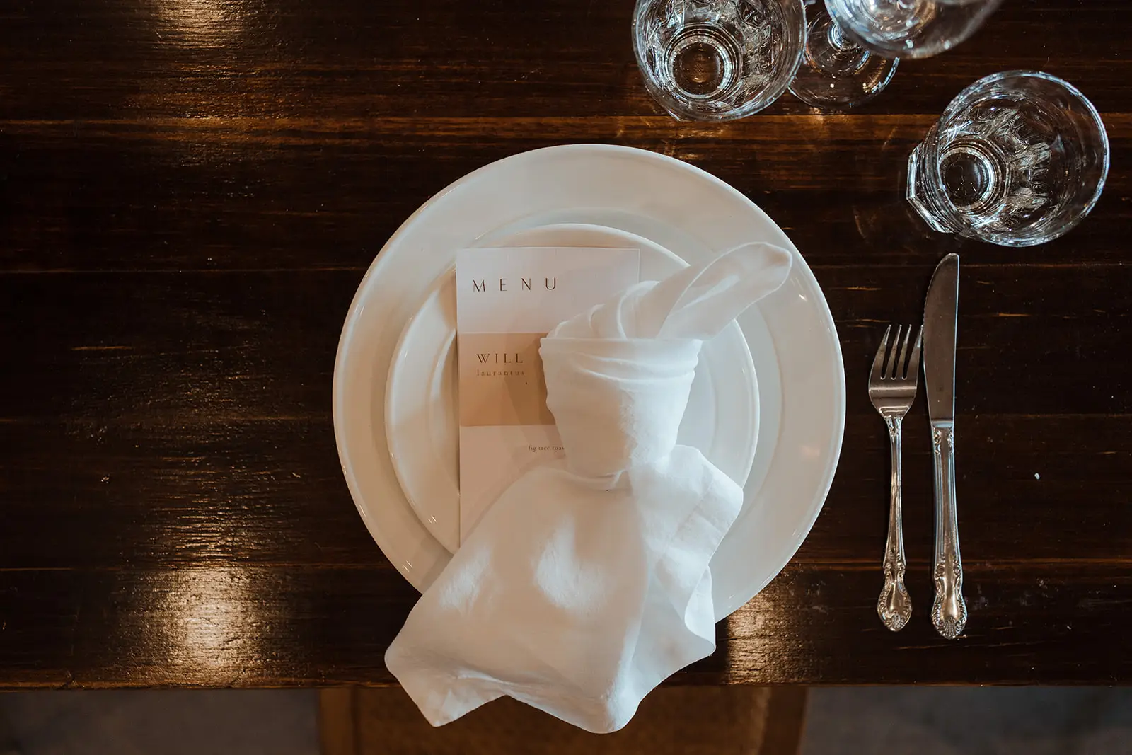 A place setting on dark timber — menu card, linen and cut glass, EarthHouse