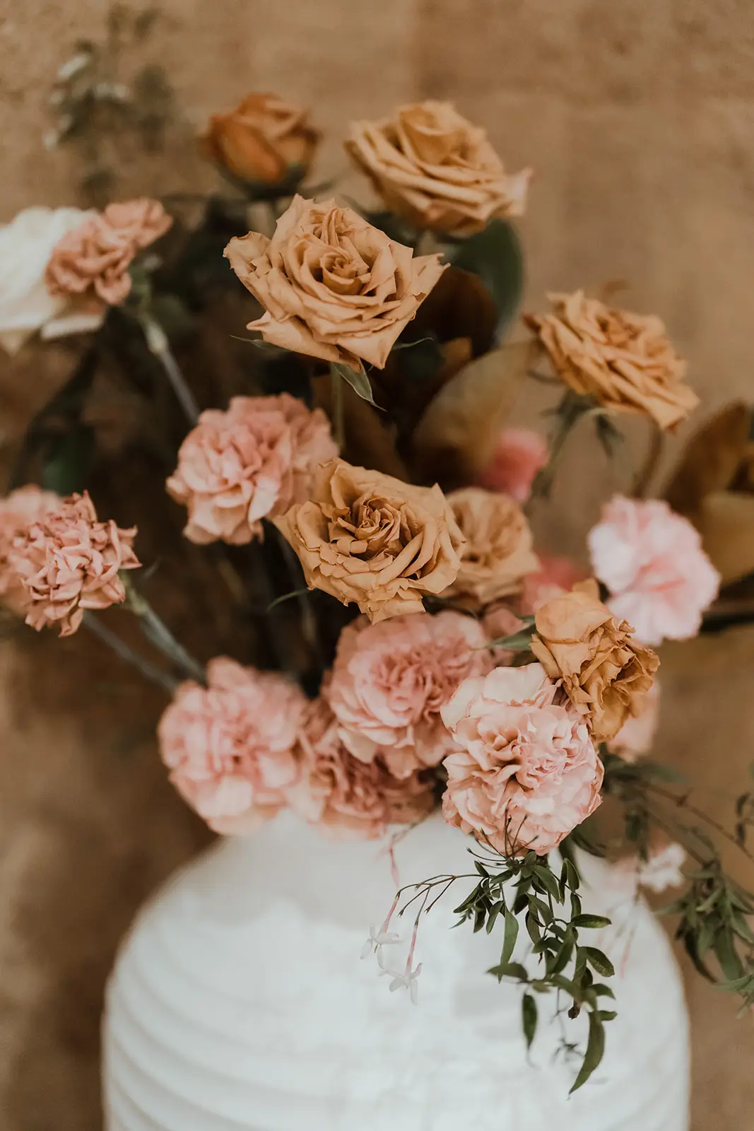 The cake dressed with tan and blush roses against the rammed-earth wall, EarthHouse