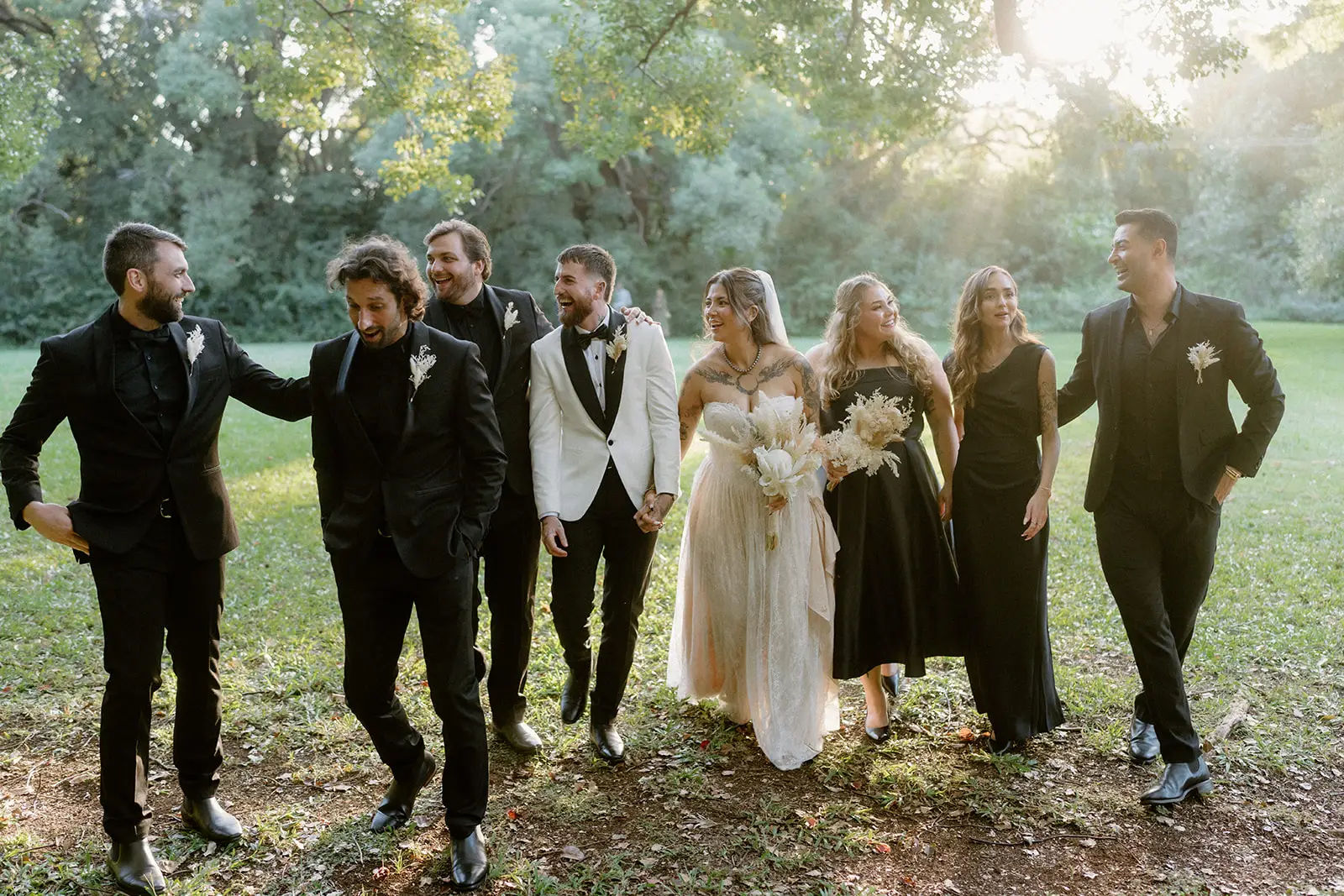 The wedding party walking the grass in backlit afternoon sun, Ewingsdale Hall