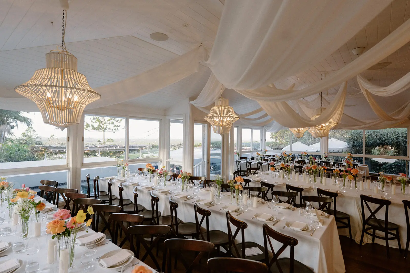 Long tables and cross-back chairs under the draped ceiling, windows open to the view, Fig Tree Restaurant