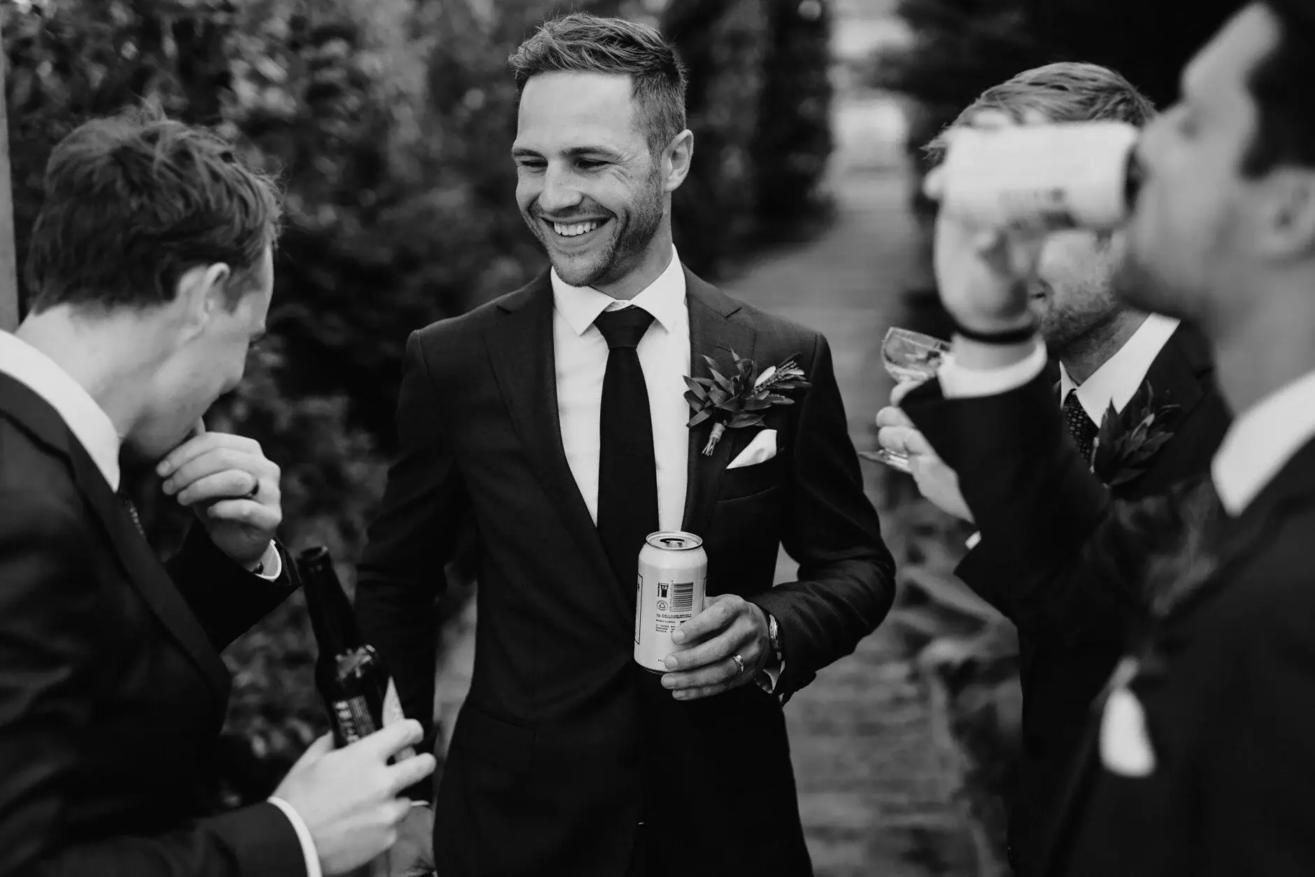 Nev laughing with a groomsman during canapés, black and white