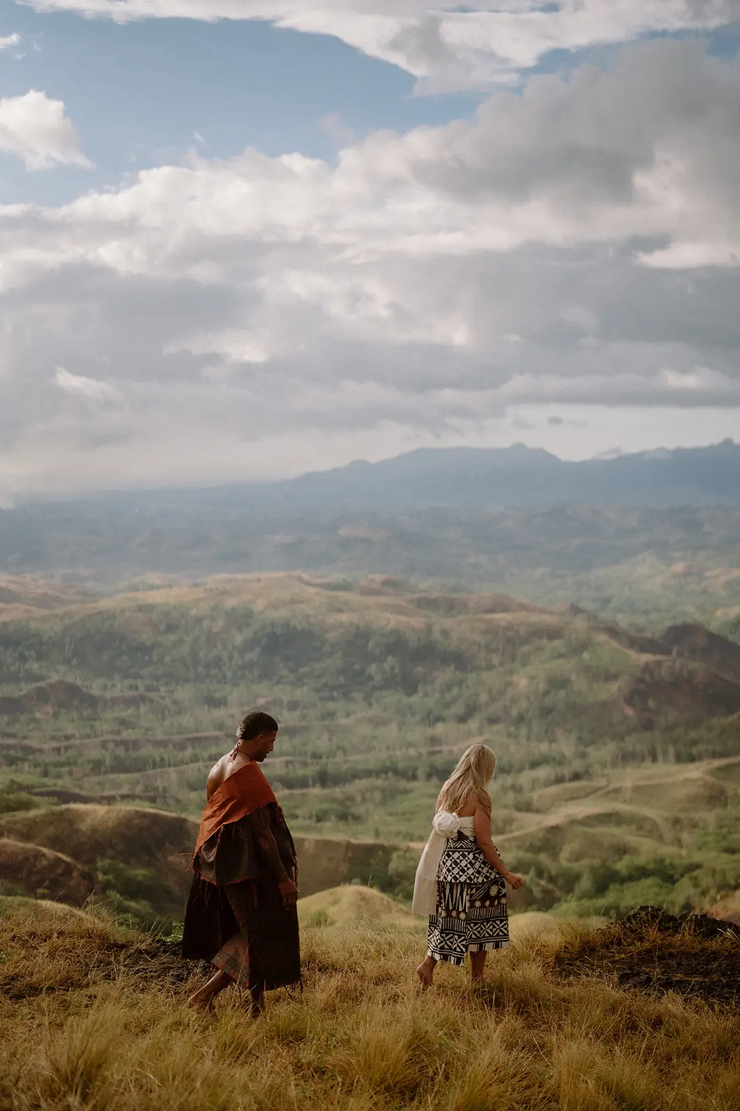 Brittany and Viliame walking through highland grass under a wide sky, Fiji