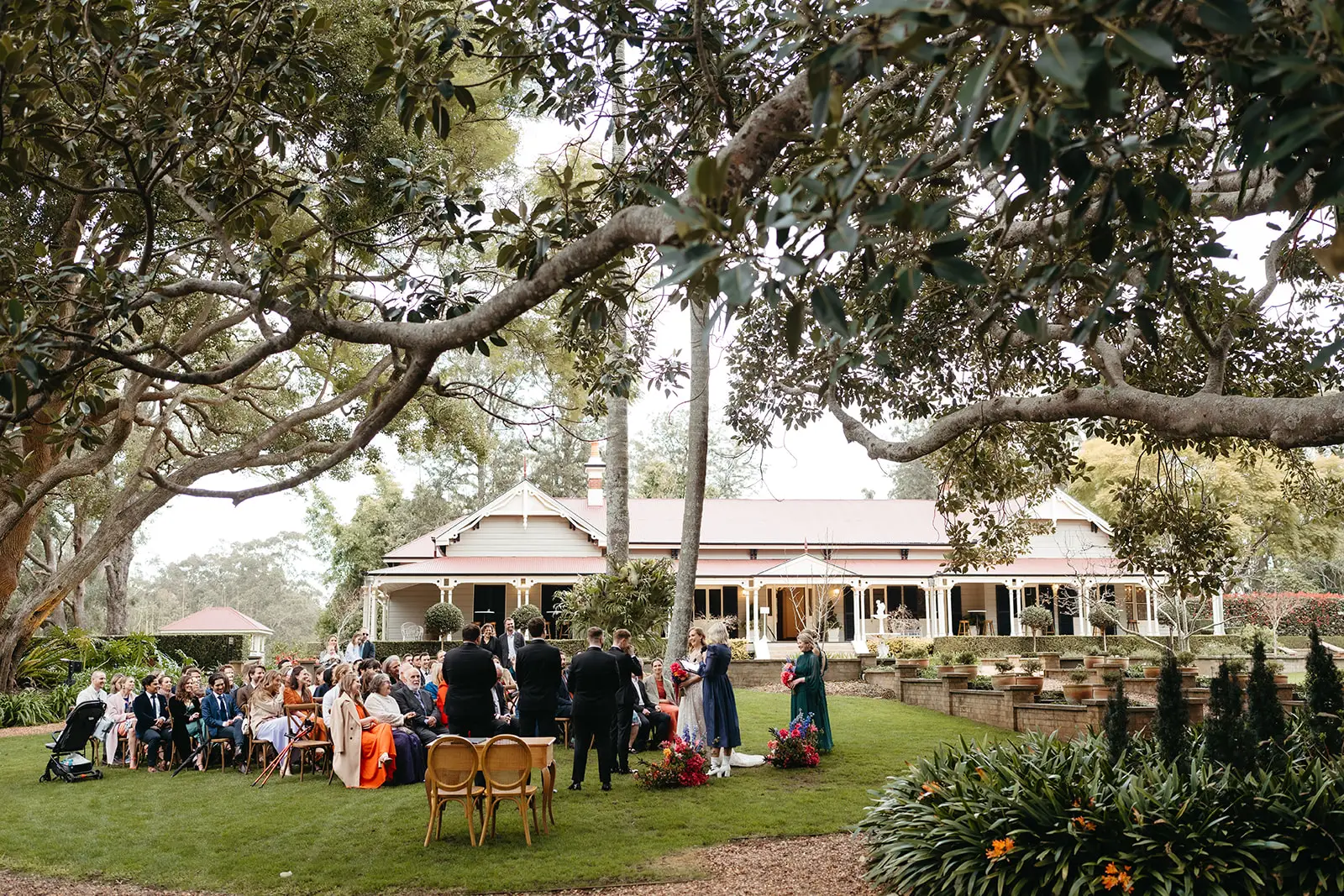 Guests seated under the fig limbs with the homestead beyond, Gabbinbar Homestead