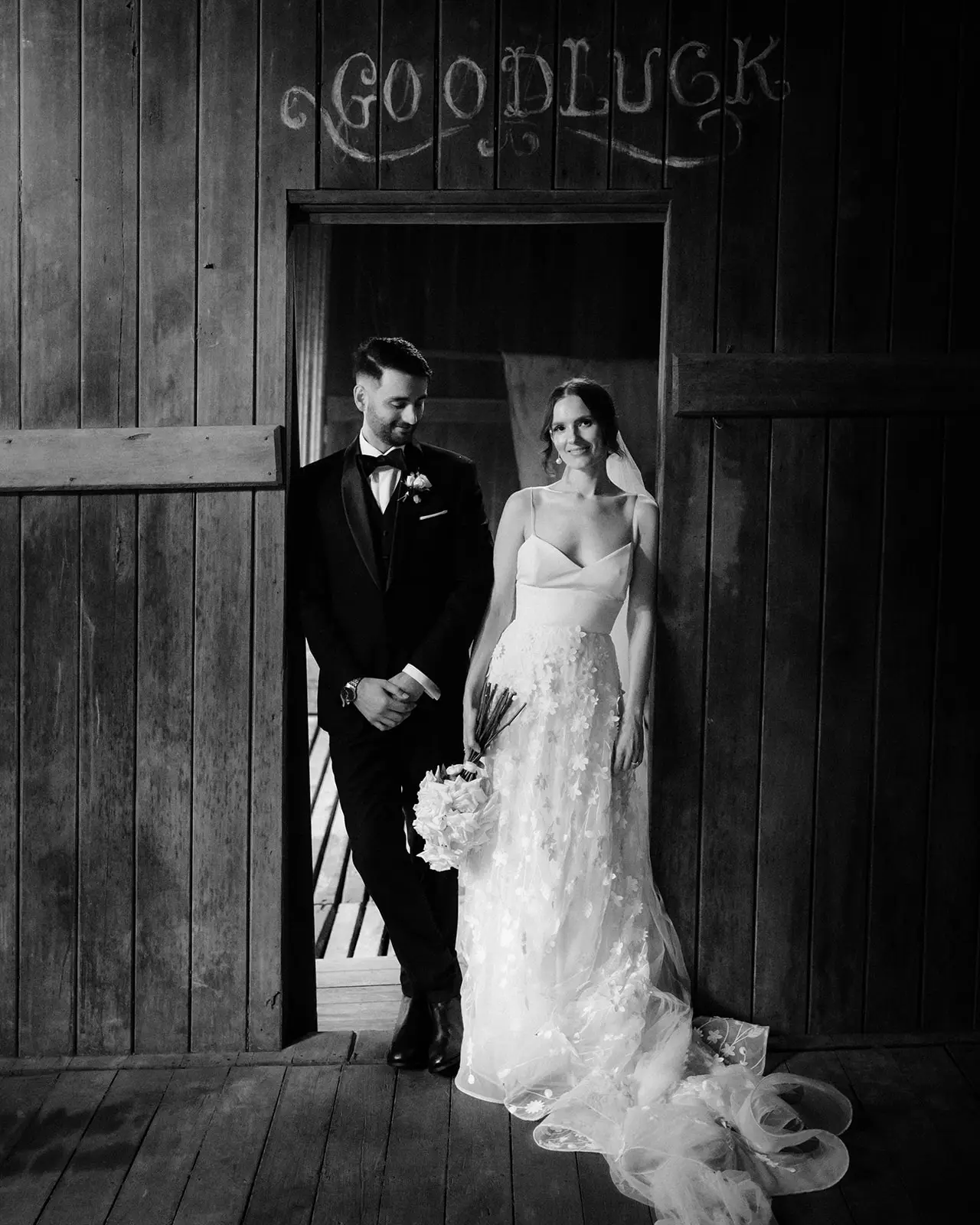 Black and white — the couple in a timber doorway with 'good luck' chalked above it