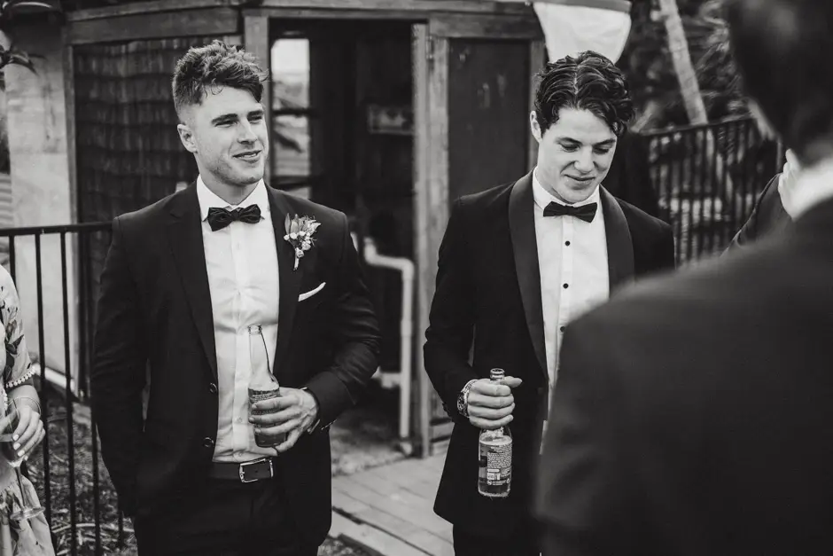 Two groomsmen in black tie with drinks outside the barn, Eureka