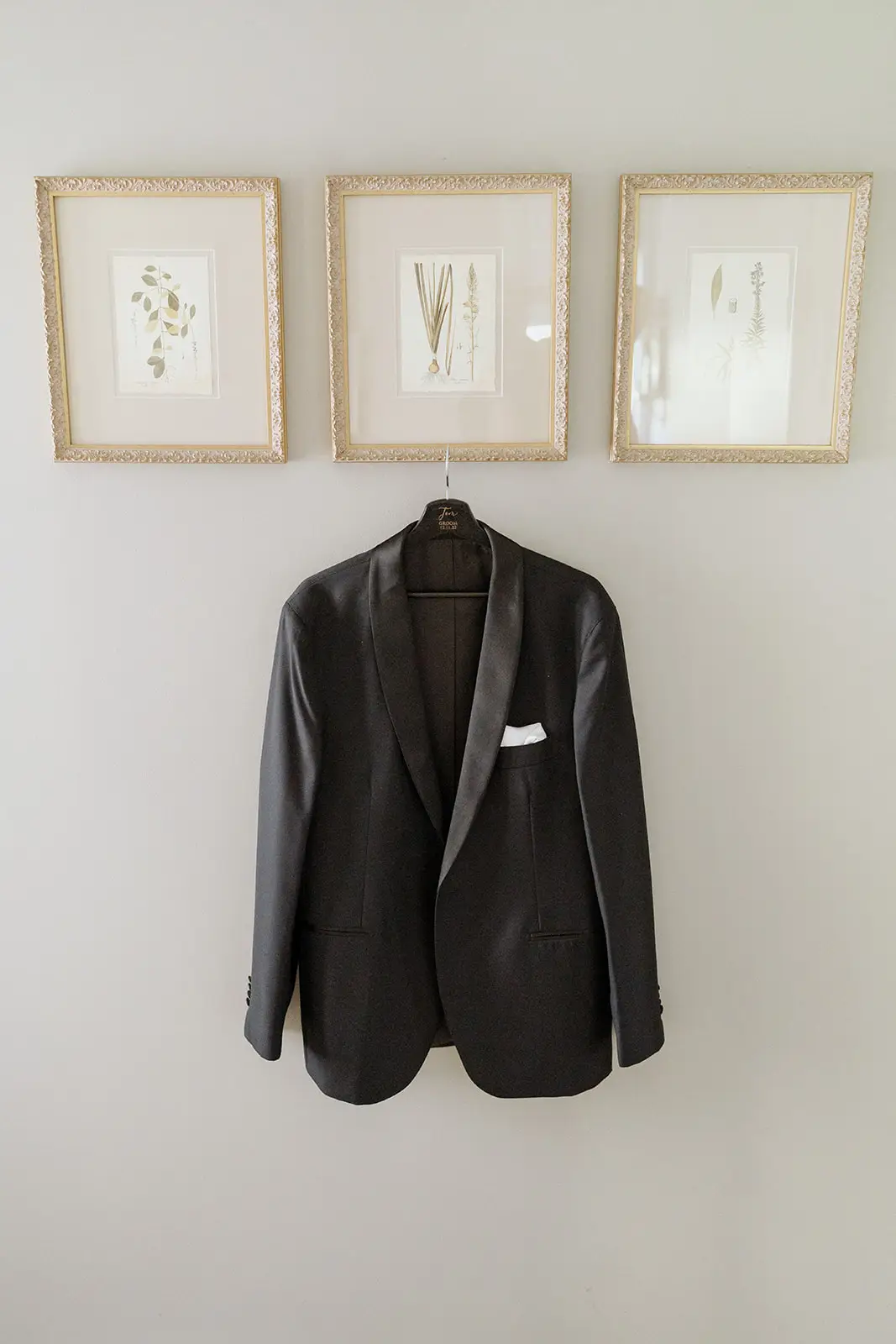 The groom's tuxedo jacket hanging beneath framed prints, Newrybar