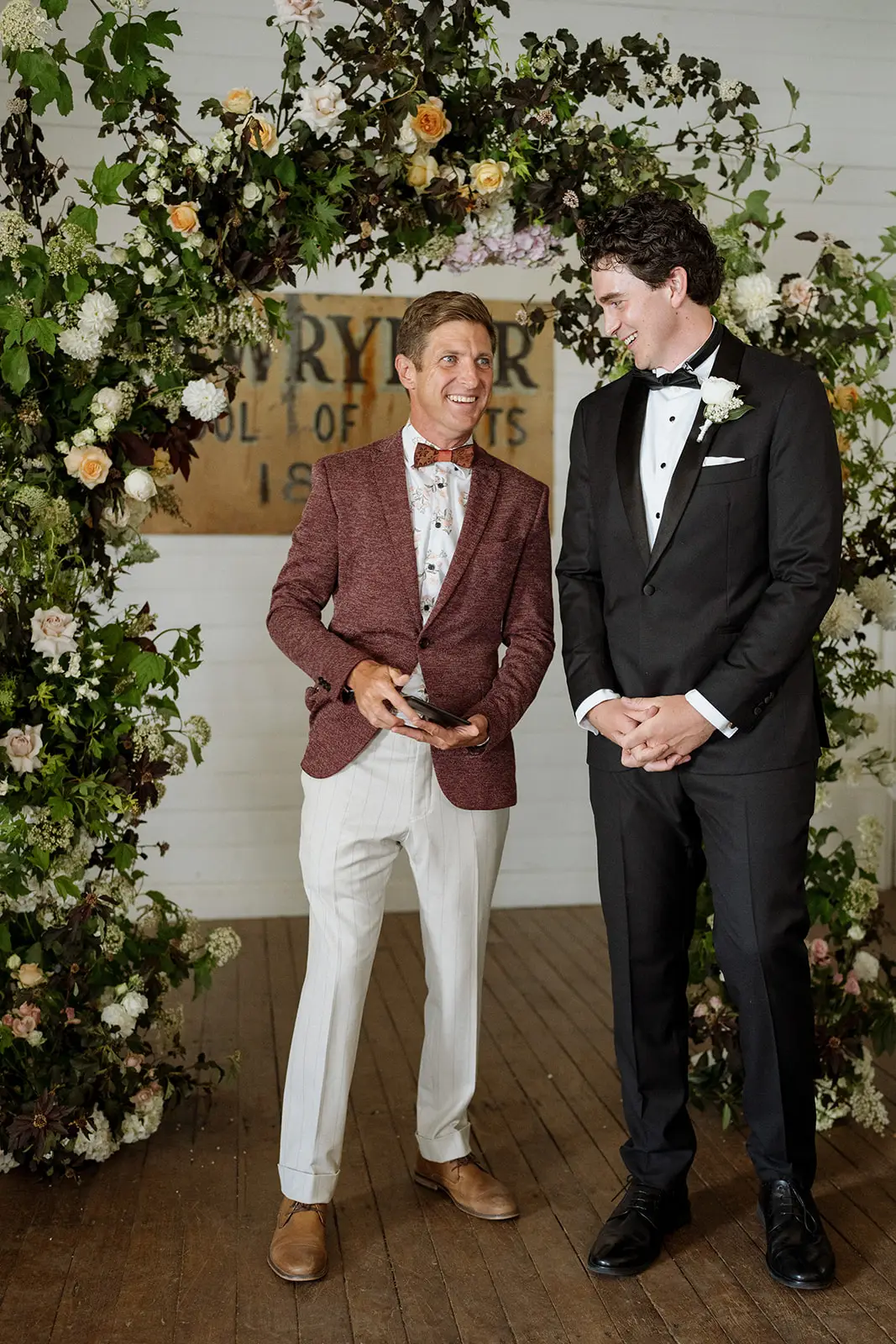 Tom and a groomsman waiting beneath the floral arch, Newrybar