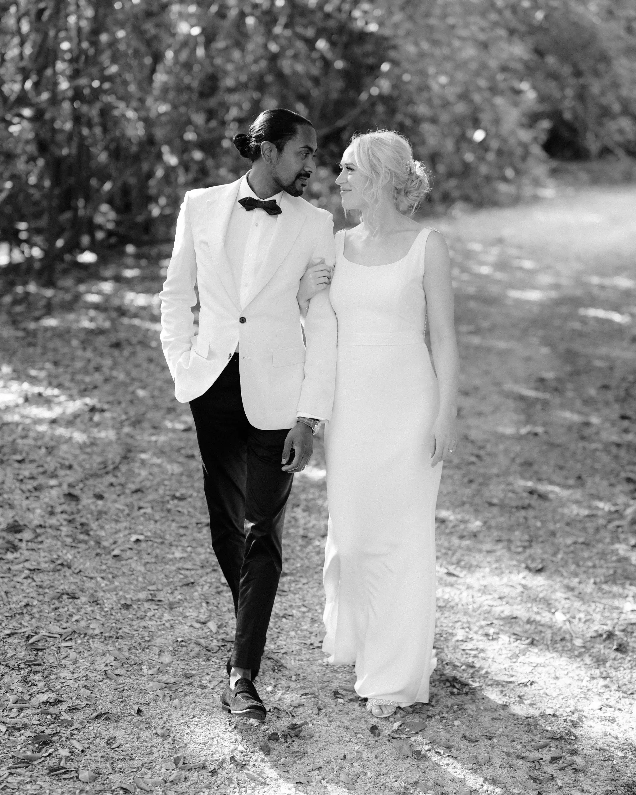 Black and white photograph of a couple walking a bush track, groom in a white dinner jacket