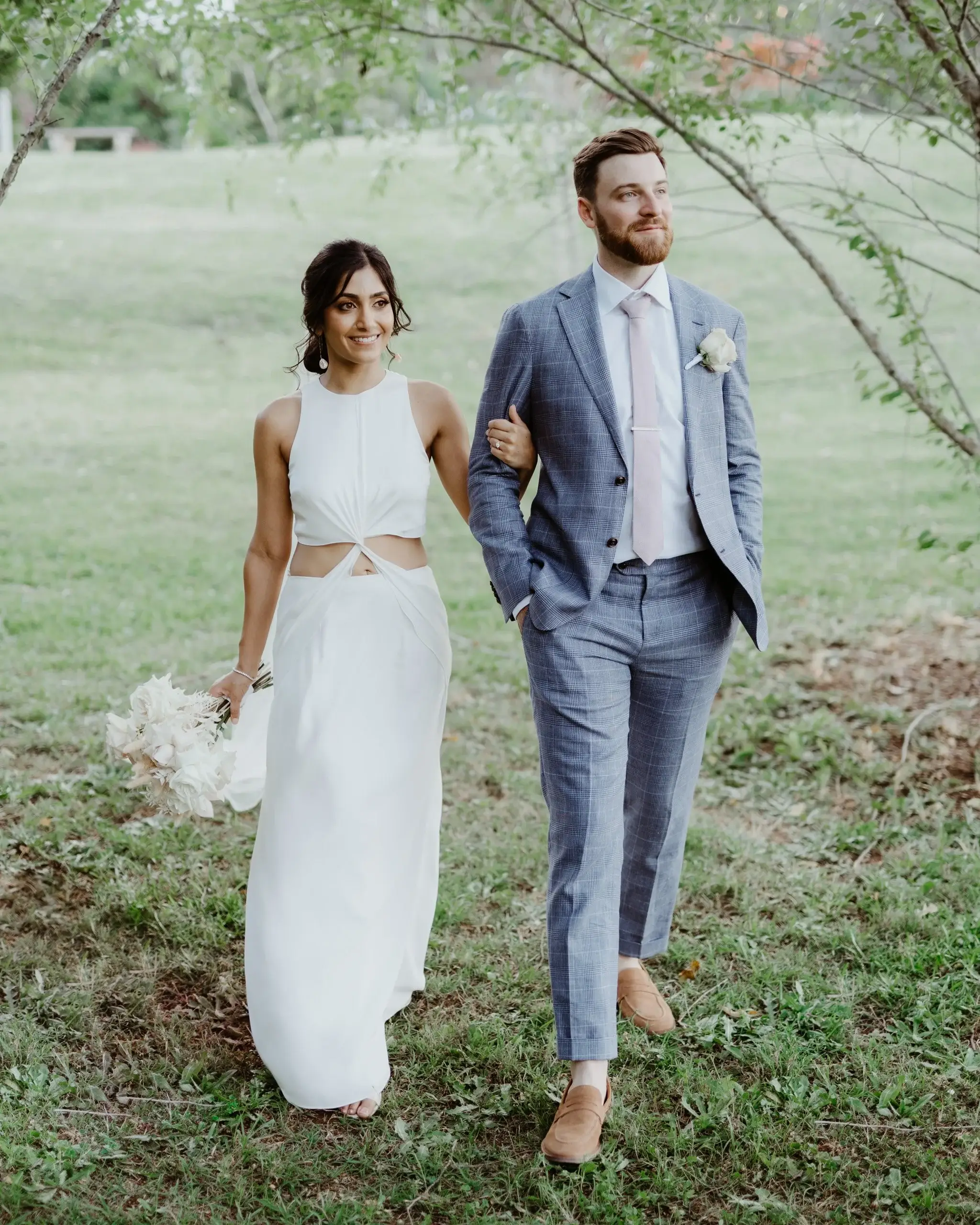 A couple walking arm in arm across a green paddock