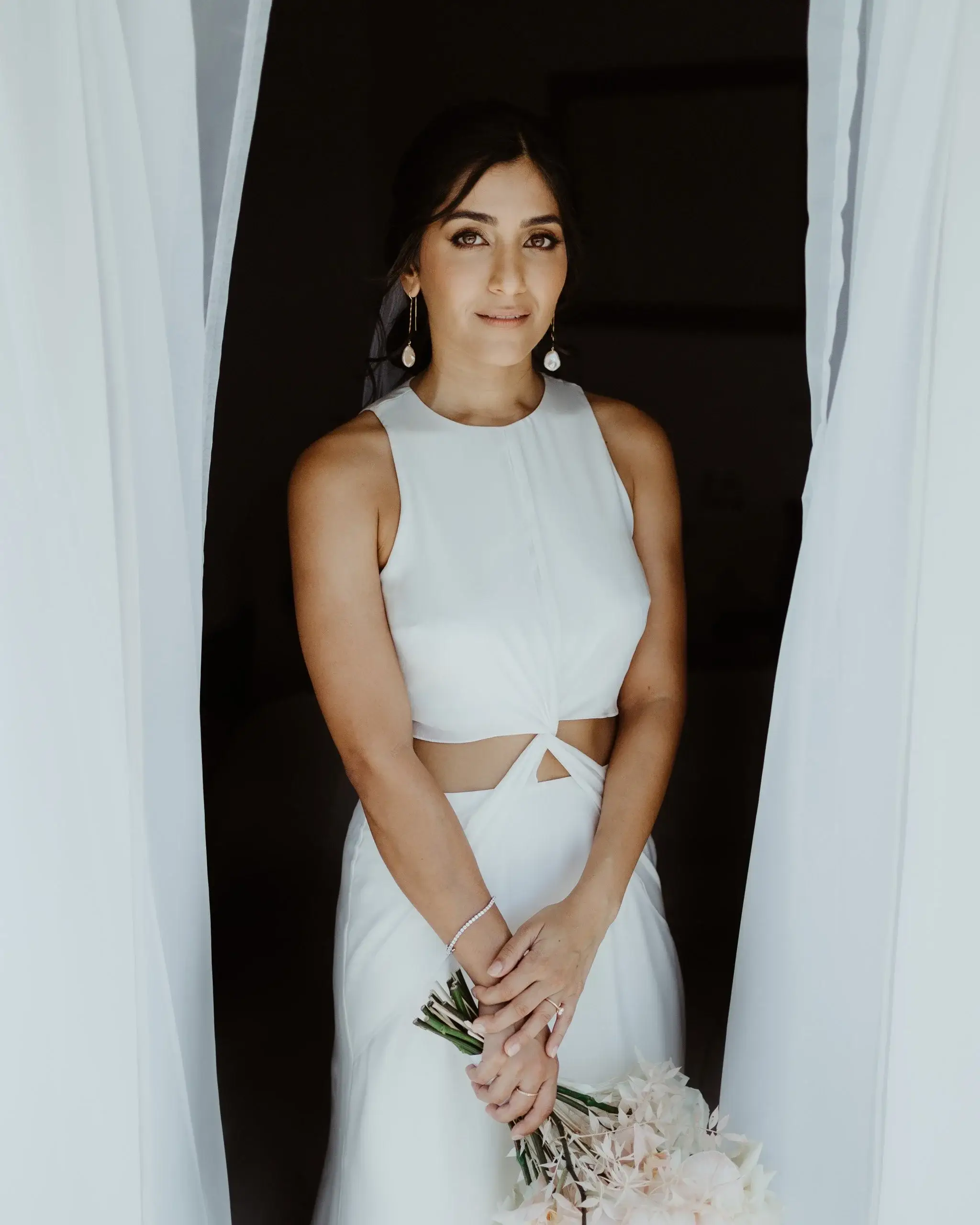 A bride standing between white curtains holding her bouquet