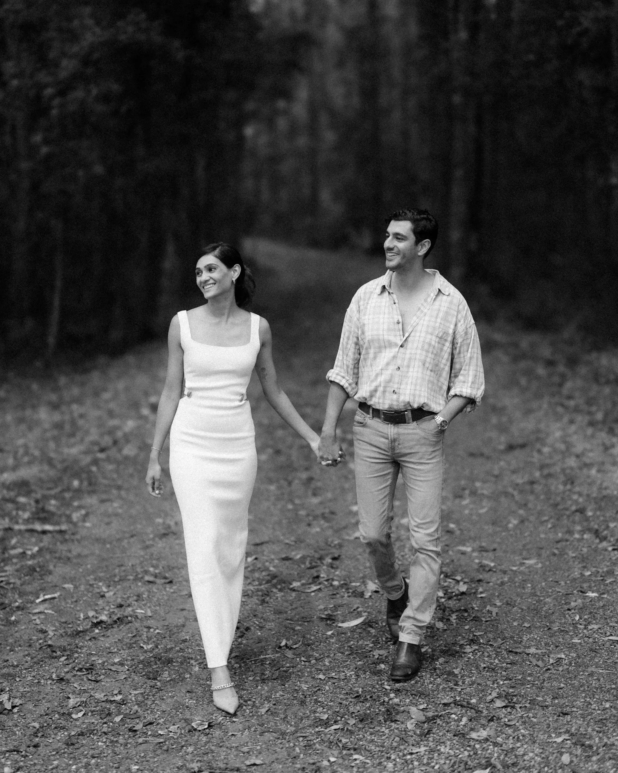 Black and white photograph of a couple walking hand in hand on a forest track