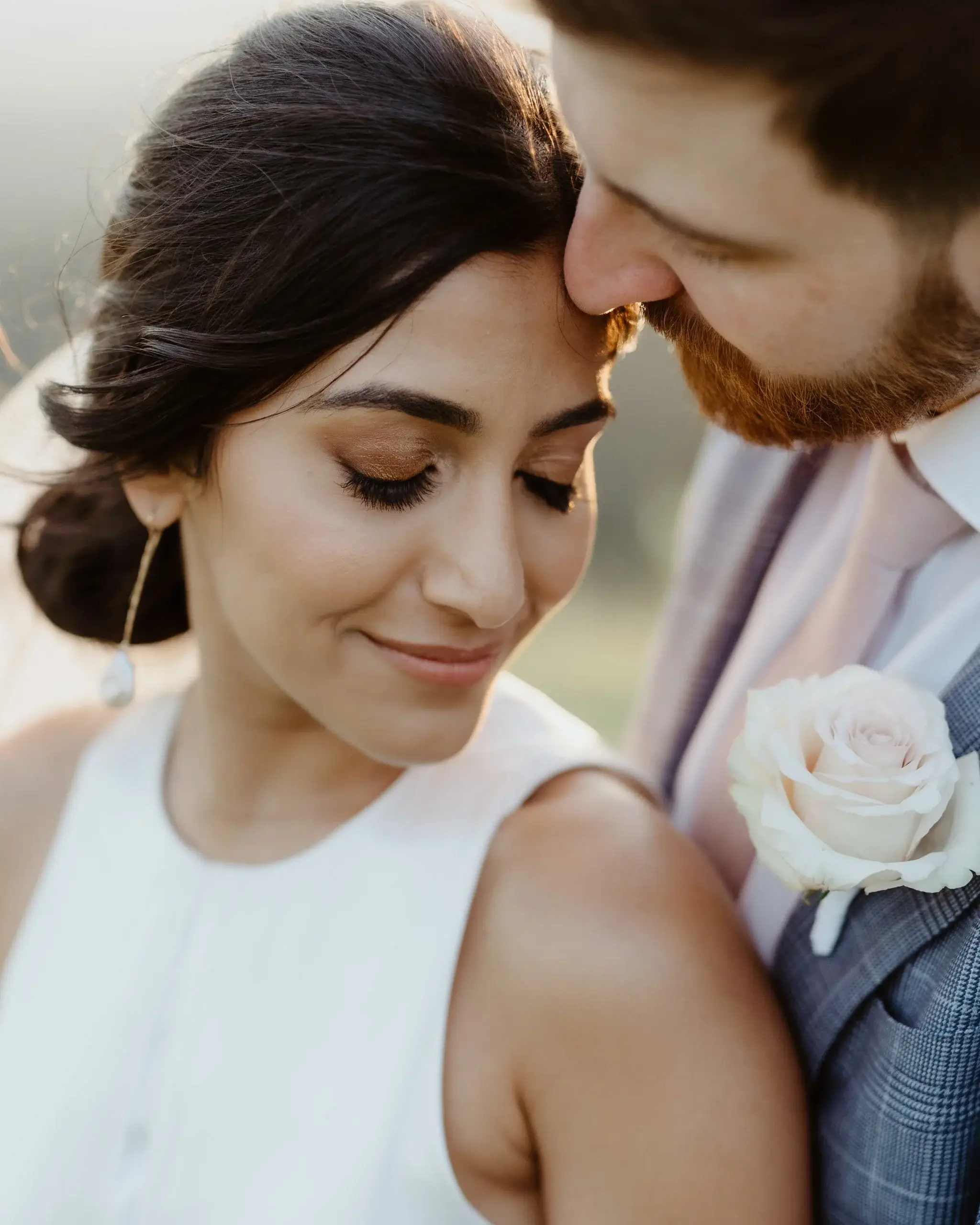 A couple close together, the bride’s eyes closed, a rose at the groom’s lapel