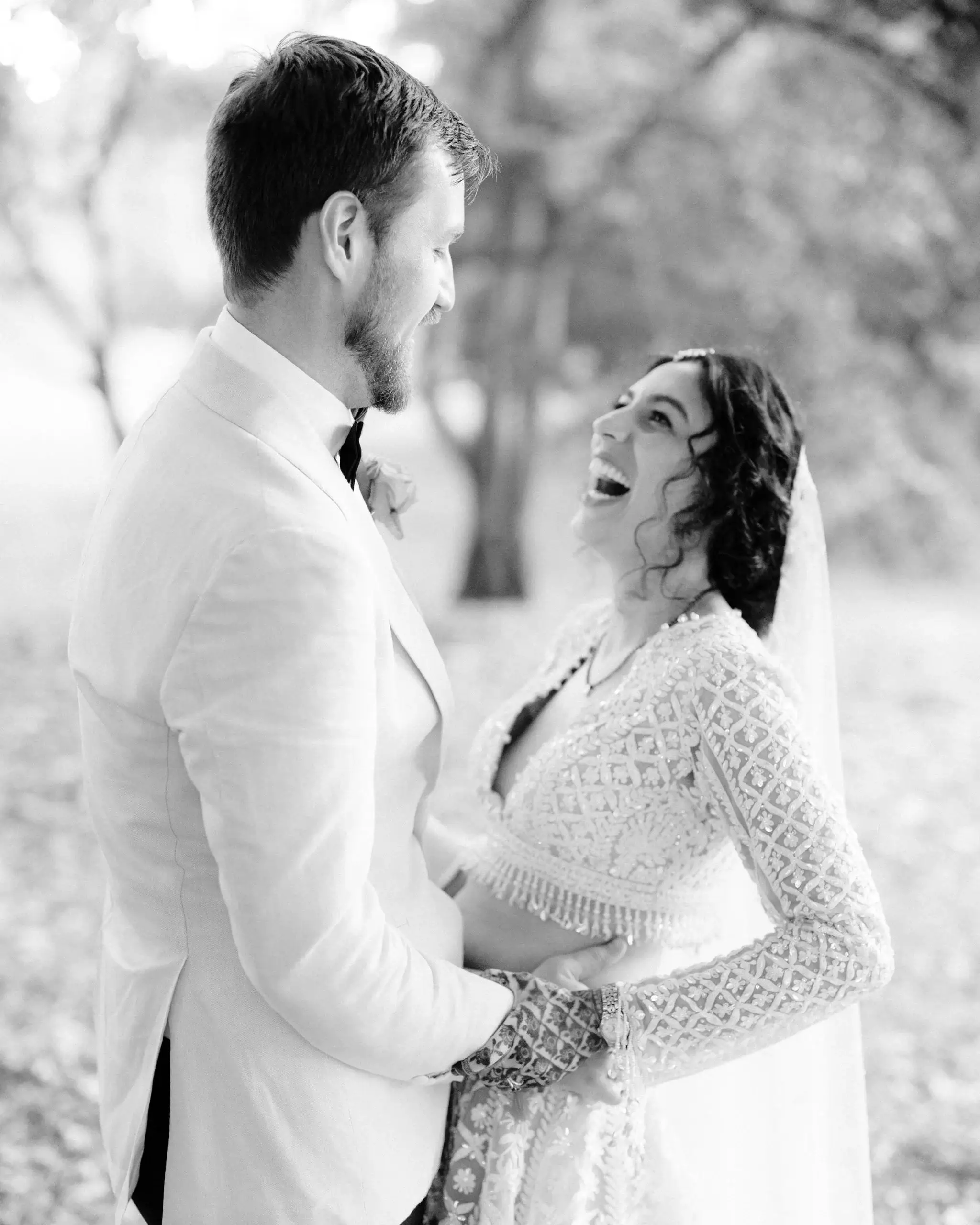 Black and white photograph of a bride looking up at her groom, both in white