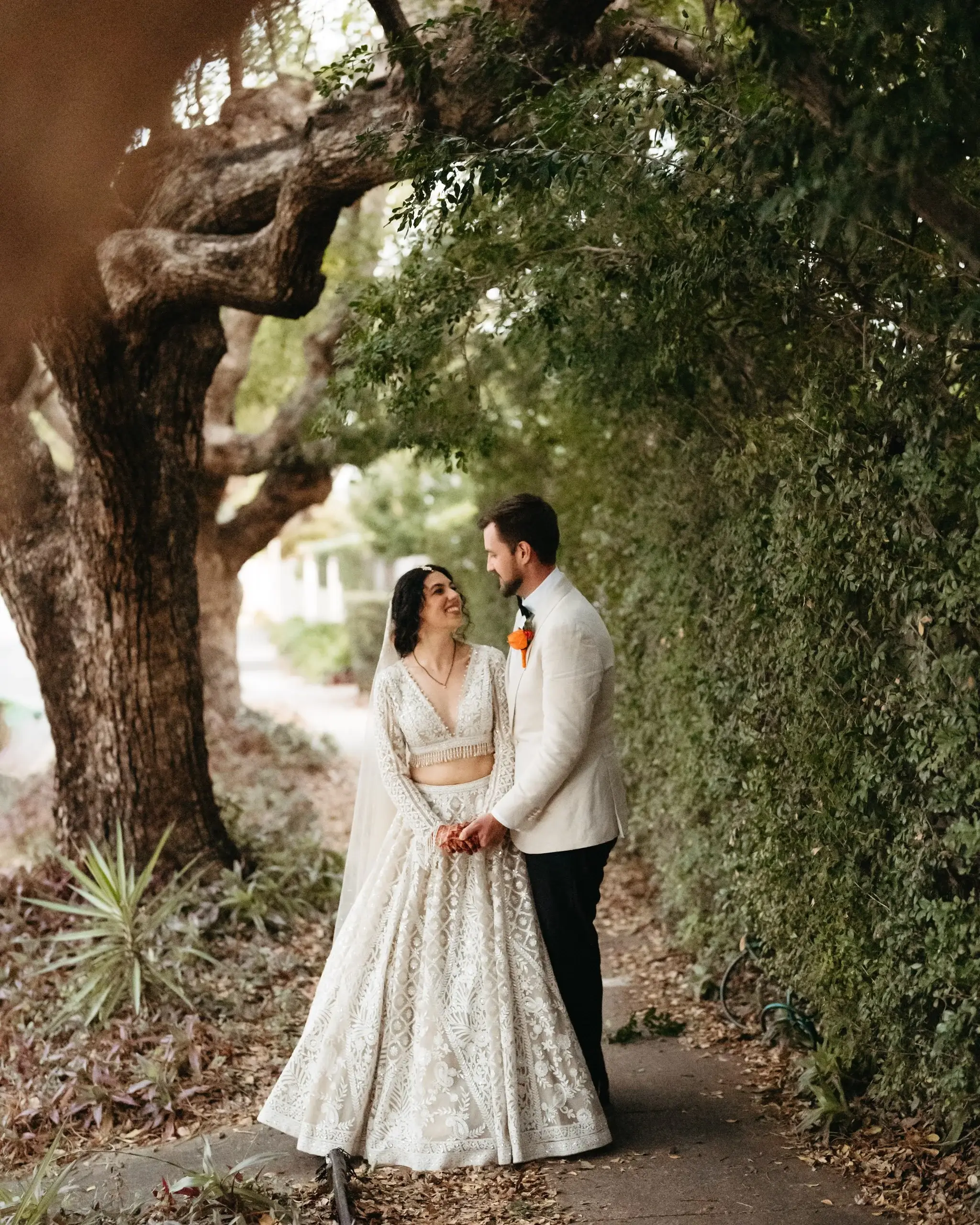 A couple in gold and cream traditional dress beneath an old fig tree