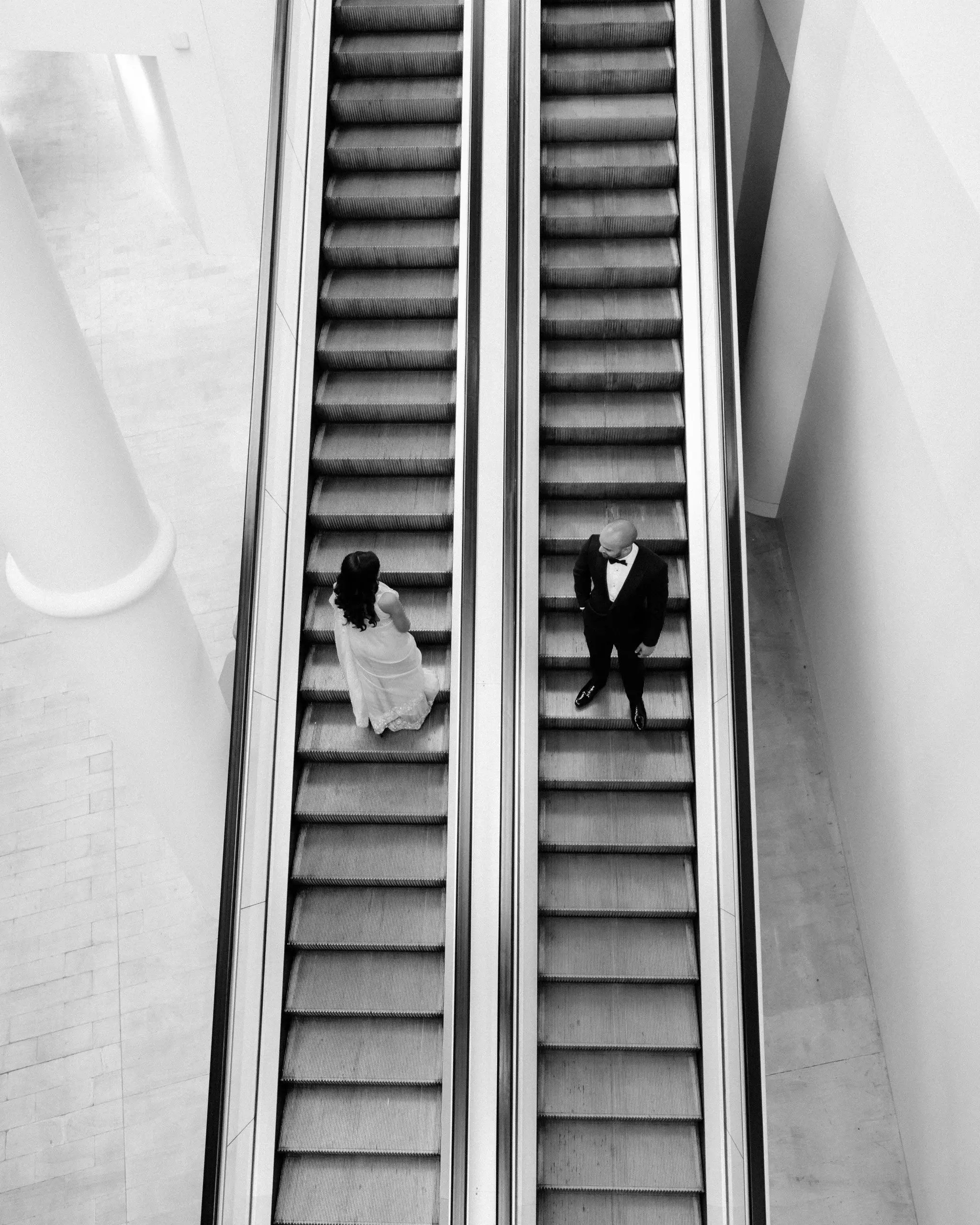 Black and white overhead photograph of a couple riding an escalator