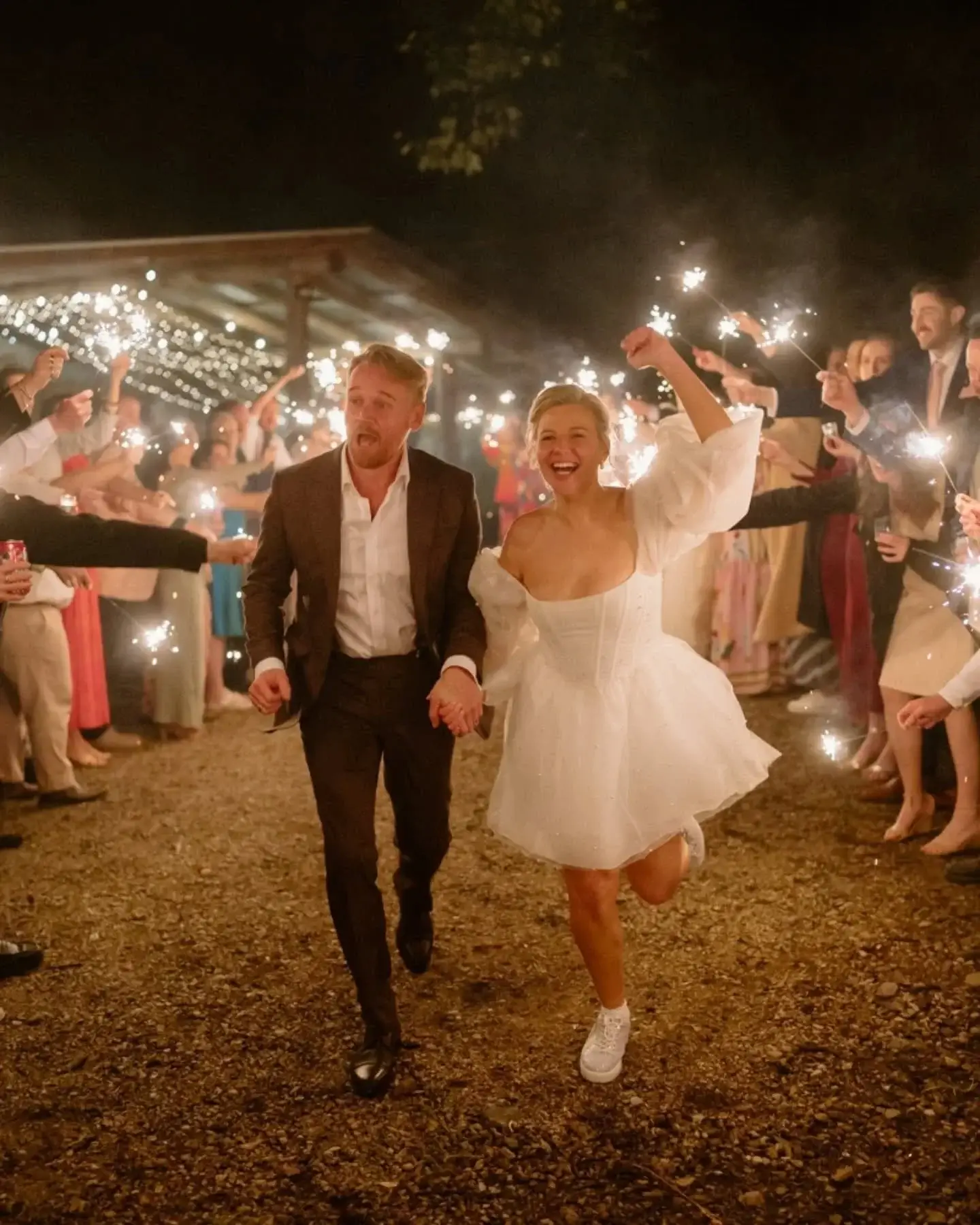 A bride and groom running hand in hand through a sparkler send-off after dark, guests cheering on both sides