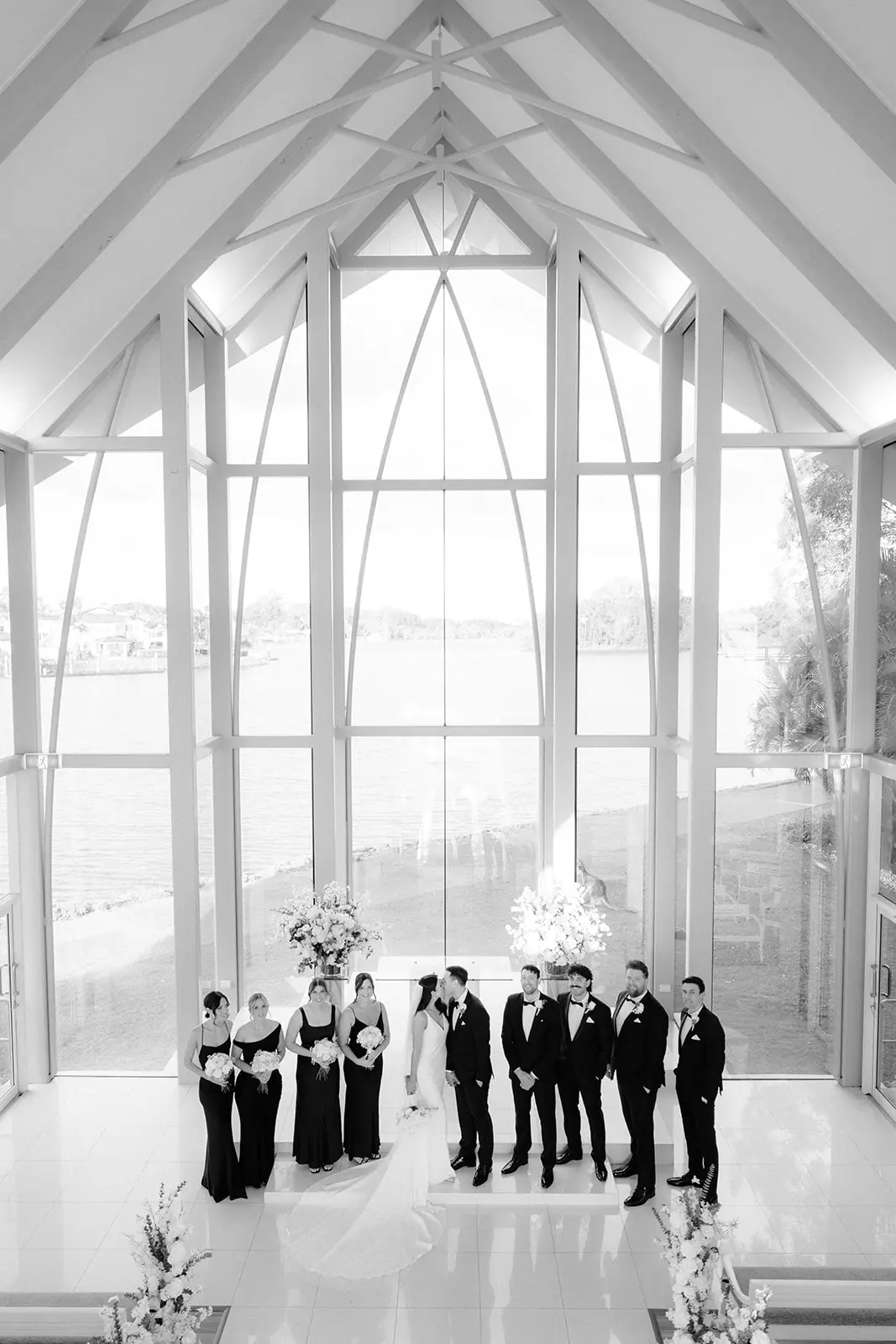 Black and white — the wedding party under the chapel’s glass gable, InterContinental Sanctuary Cove