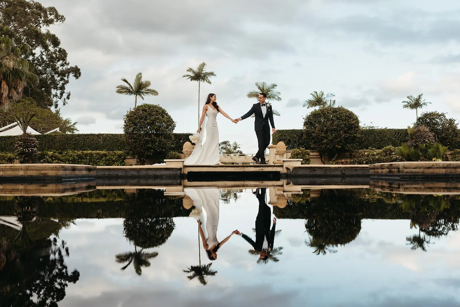 The couple mirrored in the still water of the terrace pond, palms behind, InterContinental Sanctuary Cove