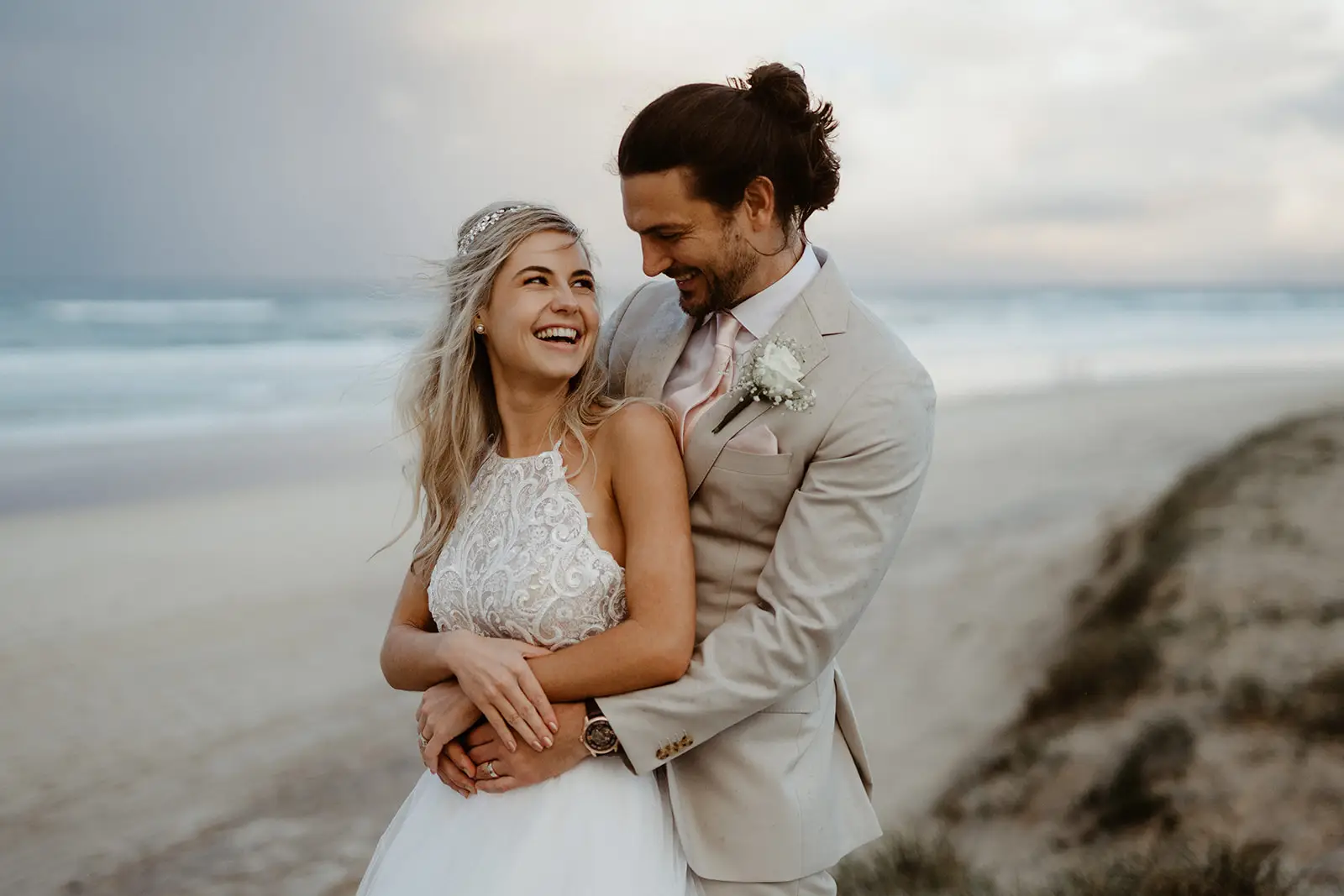 A couple laughing together on the beach in the dunes near Sanctuary Cove