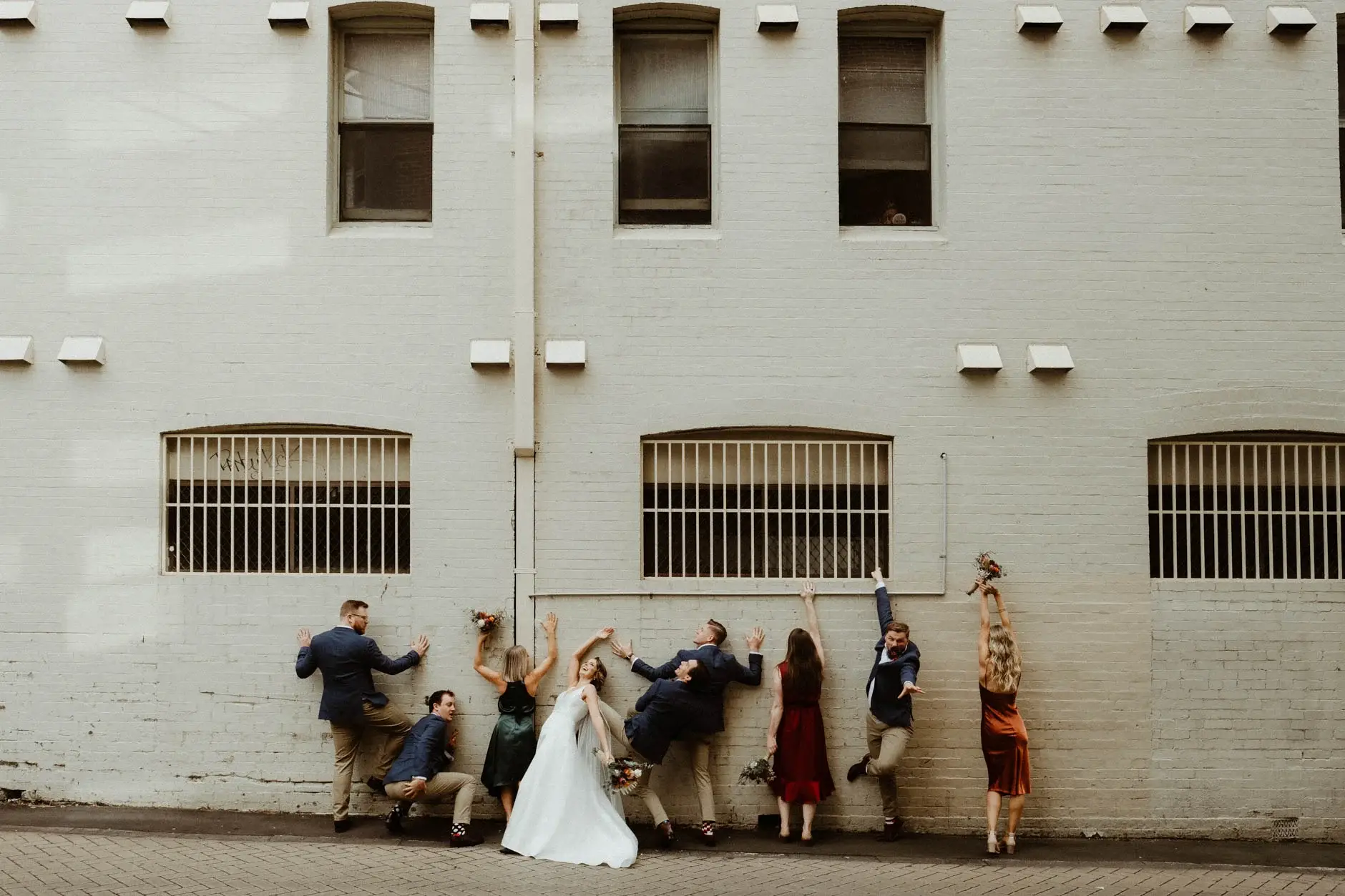 The bridal party larking about along a white brick wall, Chippendale