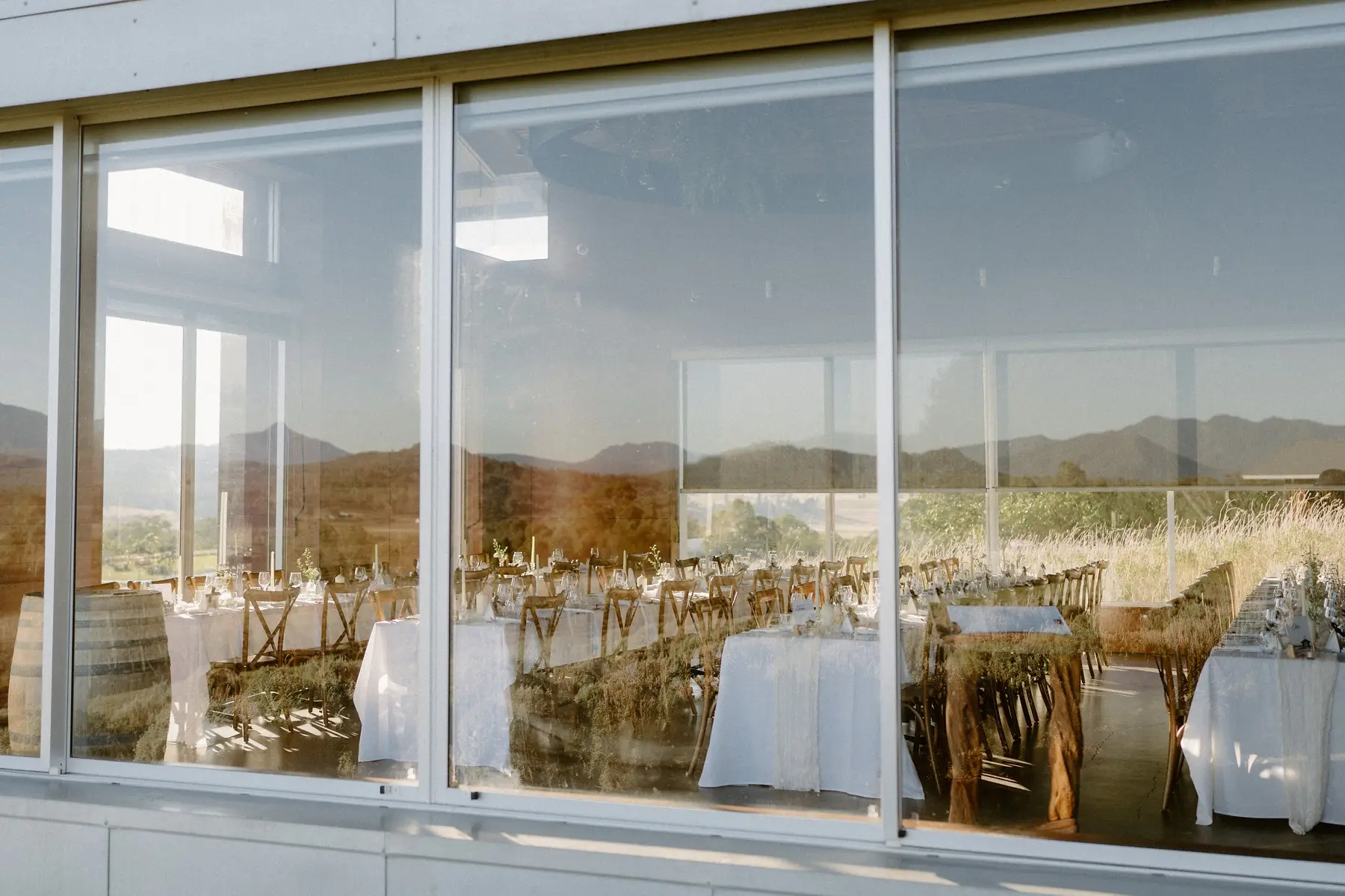 The reception room through the glass, long tables and wine barrels with the ranges reflected, Kooroomba