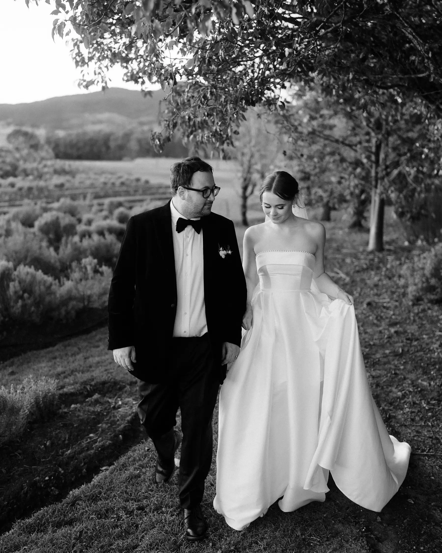 Nicole and Ryan walking hand in hand through the grove in black and white, Kooroomba Vineyard and Lavender Farm