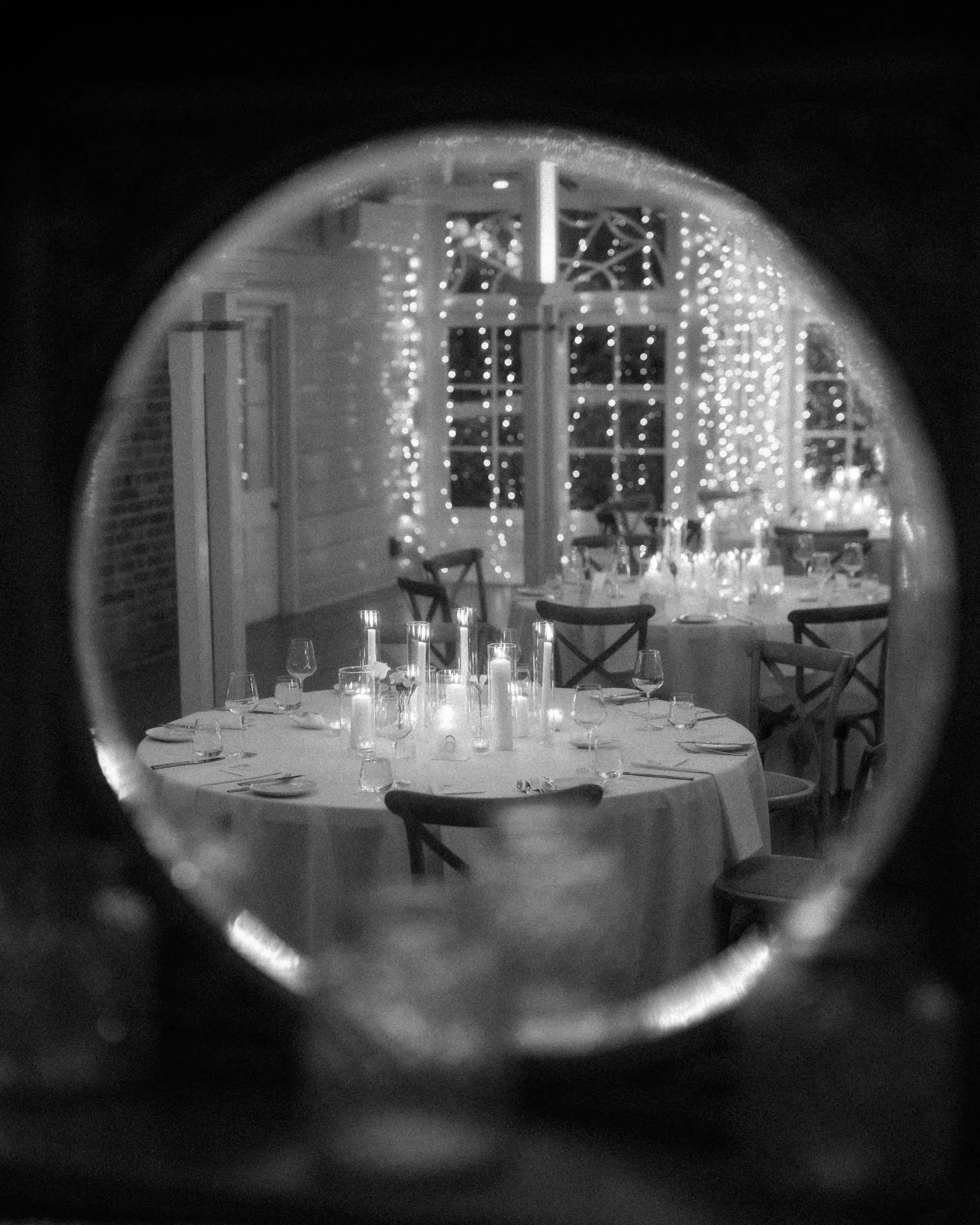 The candlelit reception tables seen through a round mirror, fairy lights in the windows behind, Gabbinbar Homestead