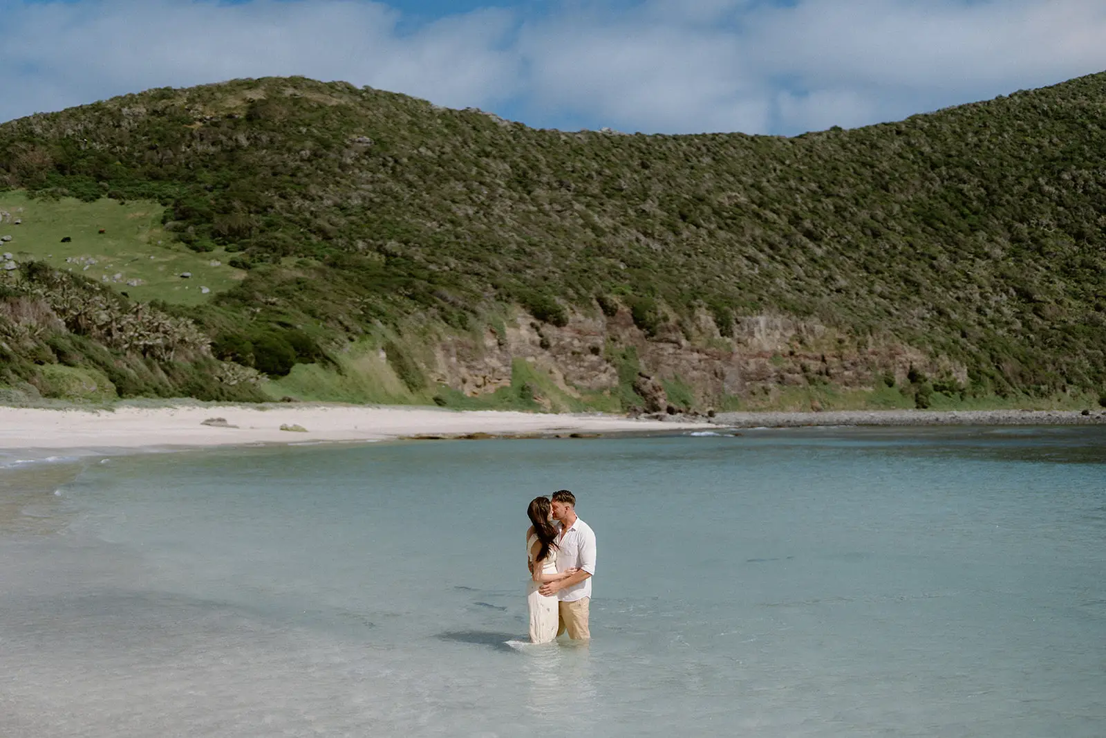 Mel and Brent embracing in the turquoise lagoon below the forested hills, Lord Howe Island
