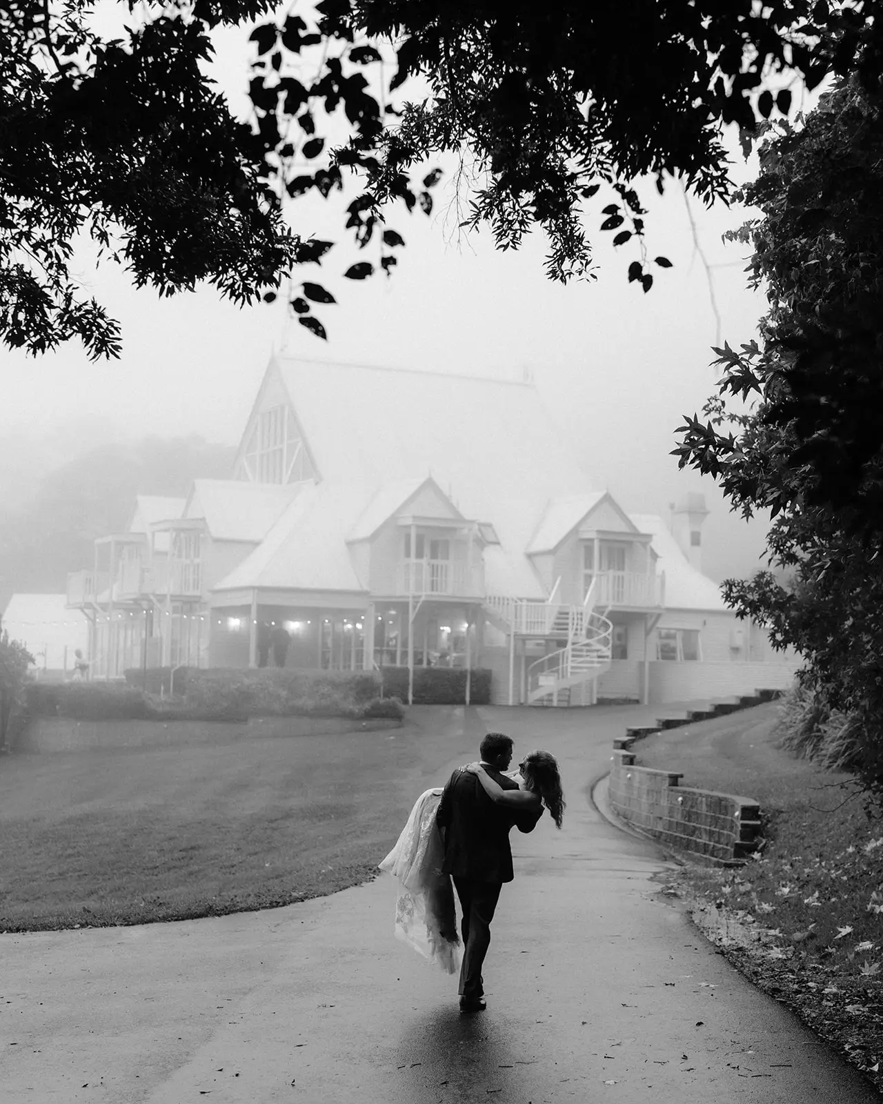 Black and white — the couple walking the drive towards the white manor in the mist, Maleny Manor