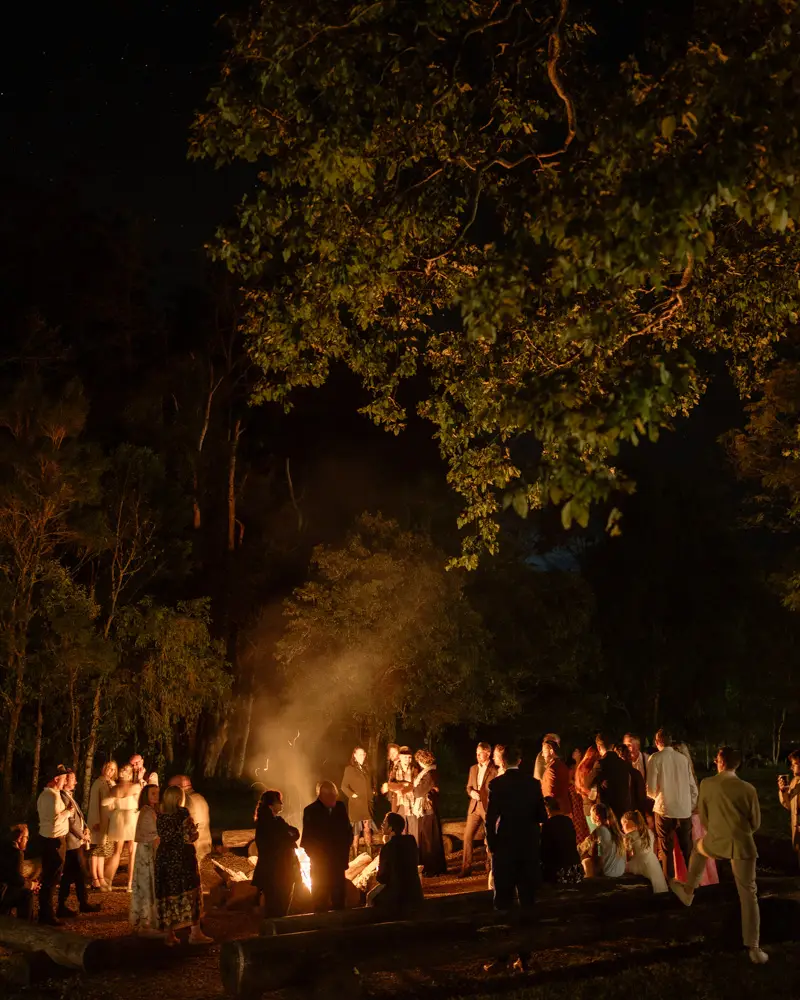 Guests gathered around a fire pit under the trees after dark, Midginbil Hill
