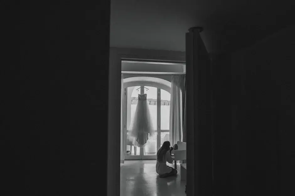 A gown hanging in a doorway down a dark hall, black and white