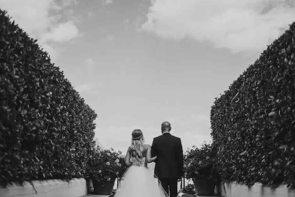 Emilie walking the aisle between clipped hedges, black and white