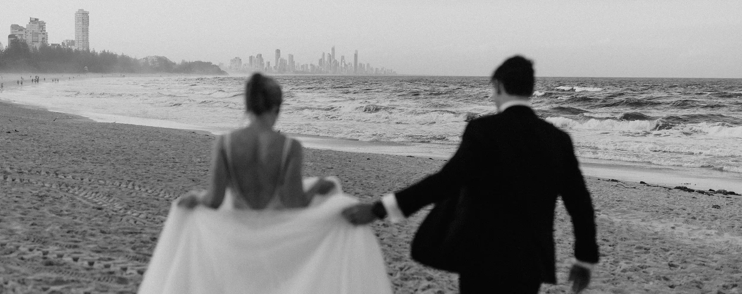 Clair and James on the beach at Burleigh Heads with the Gold Coast skyline behind them