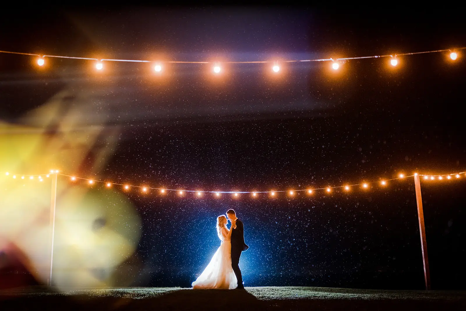 The couple under the festoons after dark, rain showing in the light, Rosewood Estate