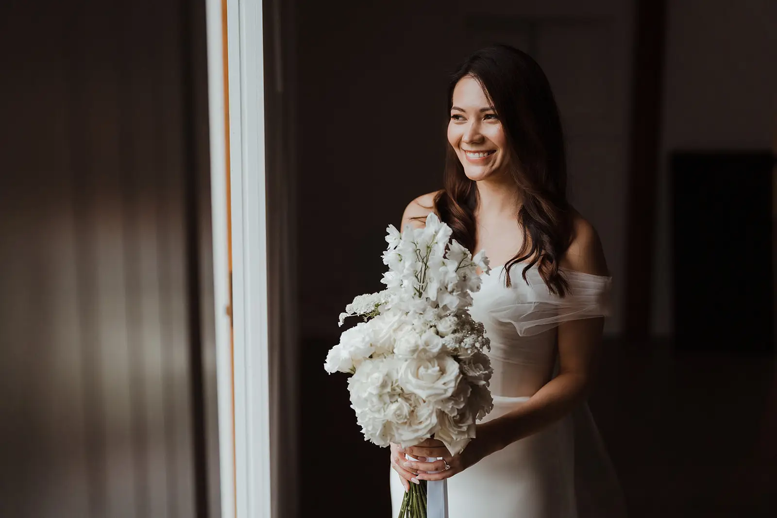 The bride with her bouquet in the doorway light, Summergrove Estate