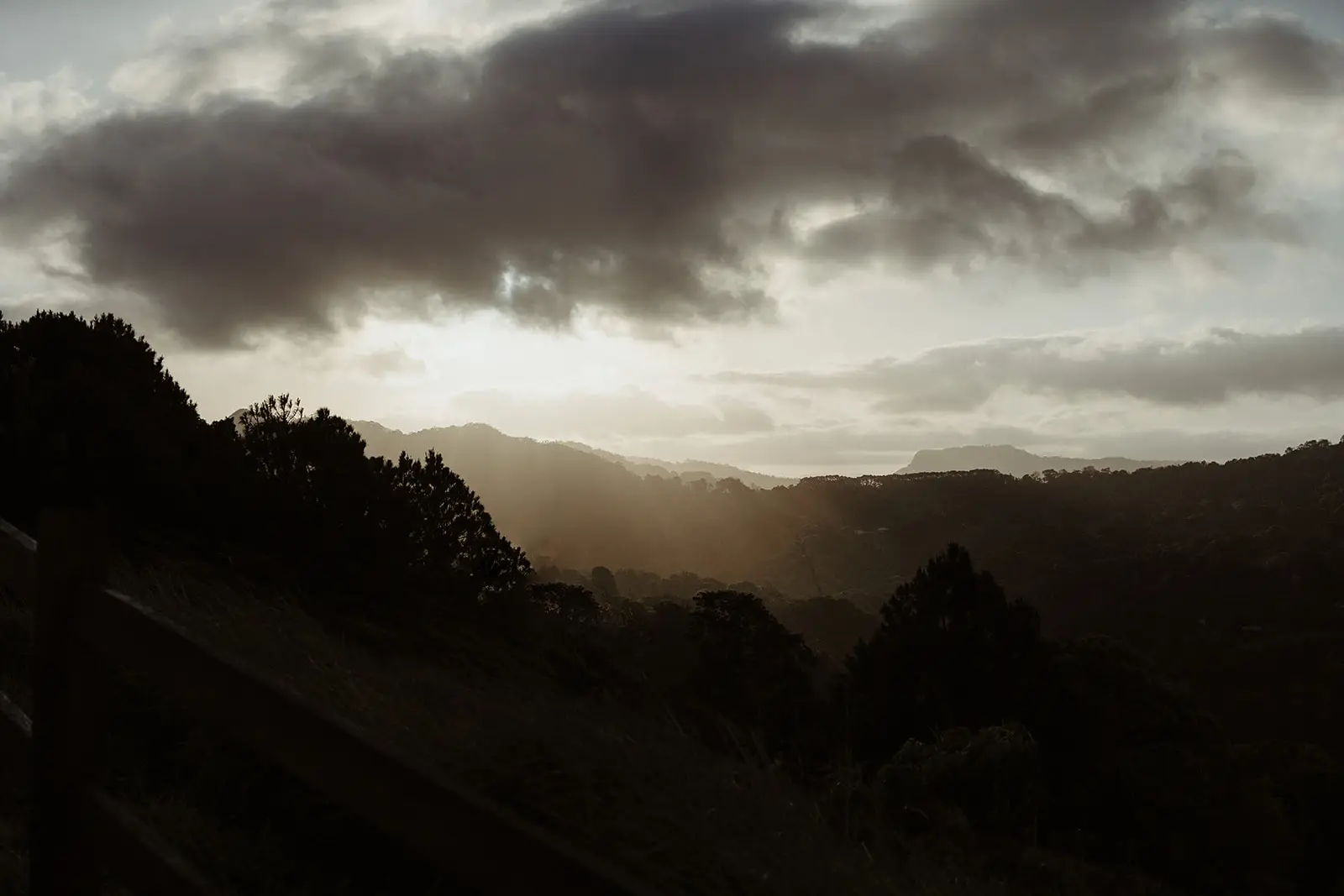 Sun breaking under heavy cloud over the ranges, seen from the fence line, Summergrove Estate