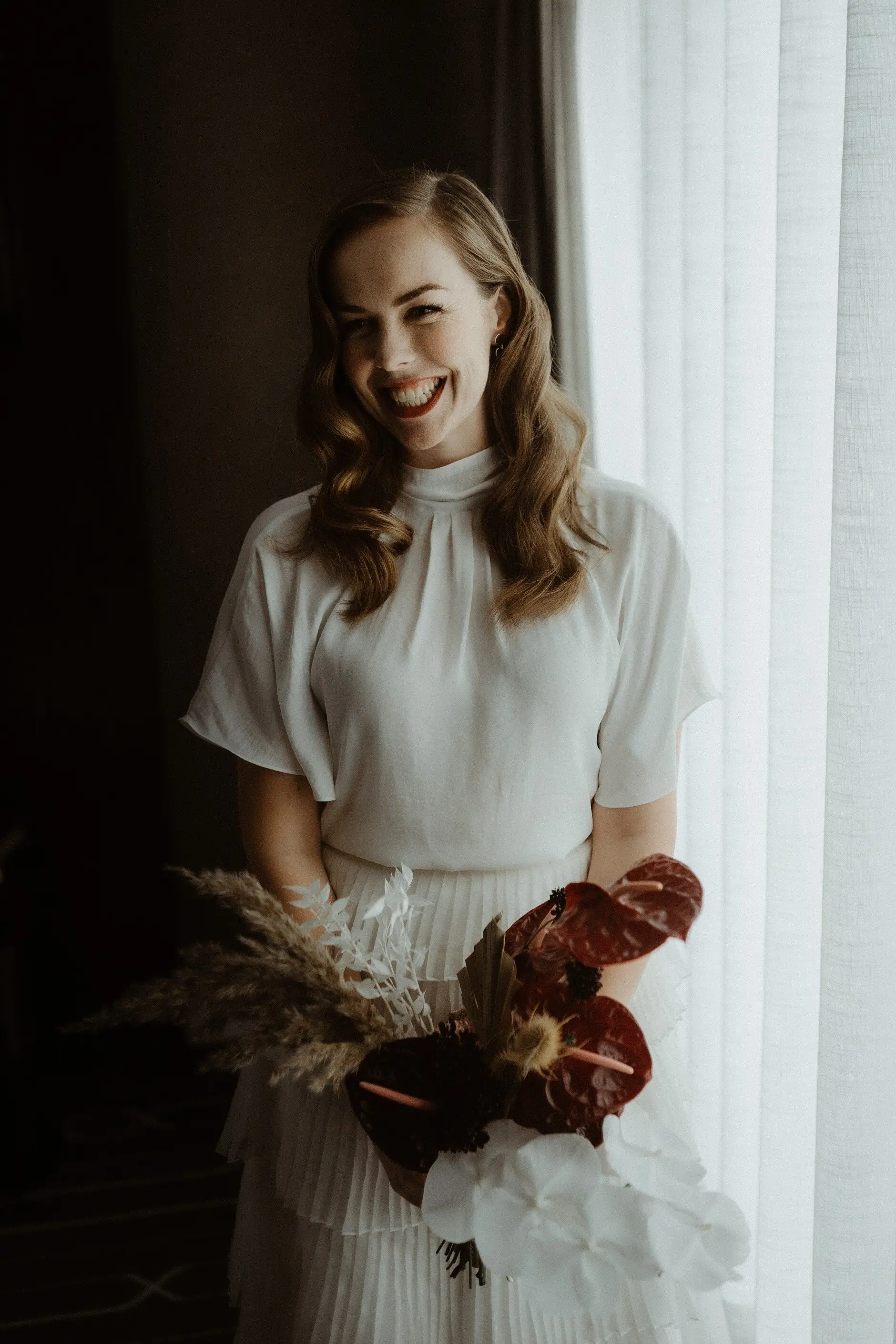 Sophie by the curtain holding her rust-red and dried-flower bouquet, Sydney