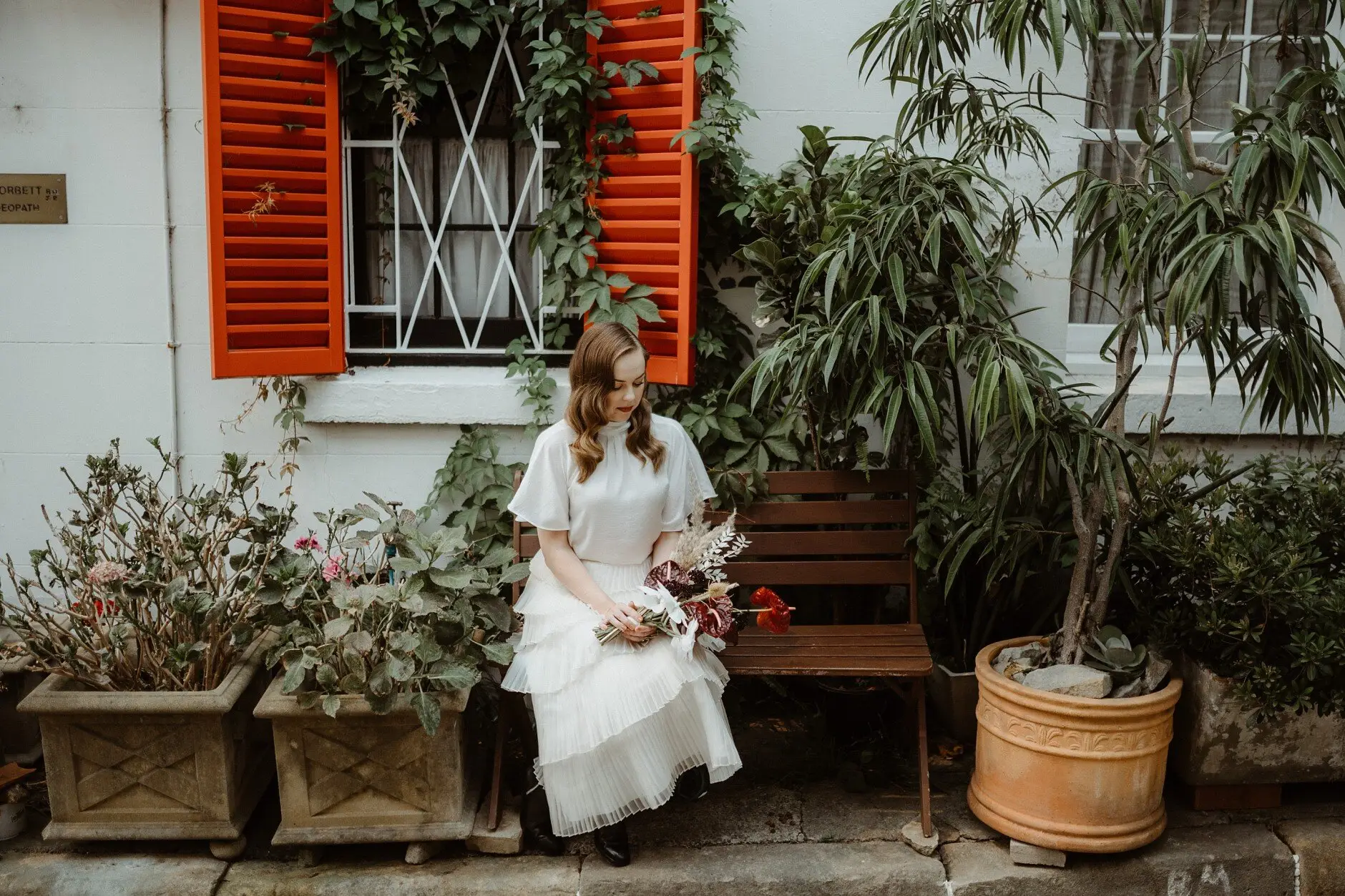 Sophie sitting on a bench beneath orange shutters and potted plants, Surry Hills