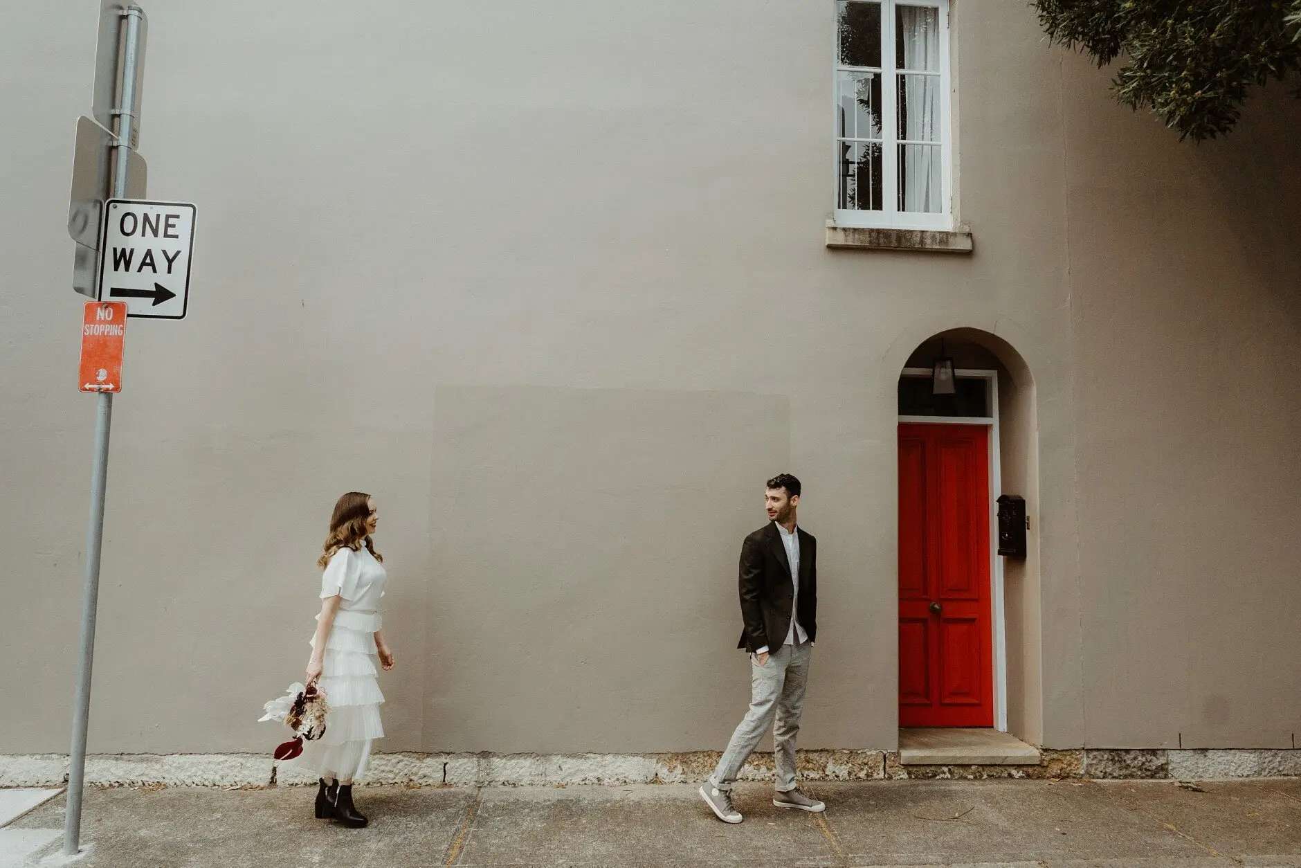 Sophie and Jonathan passing a red door in a cream terrace wall, Surry Hills