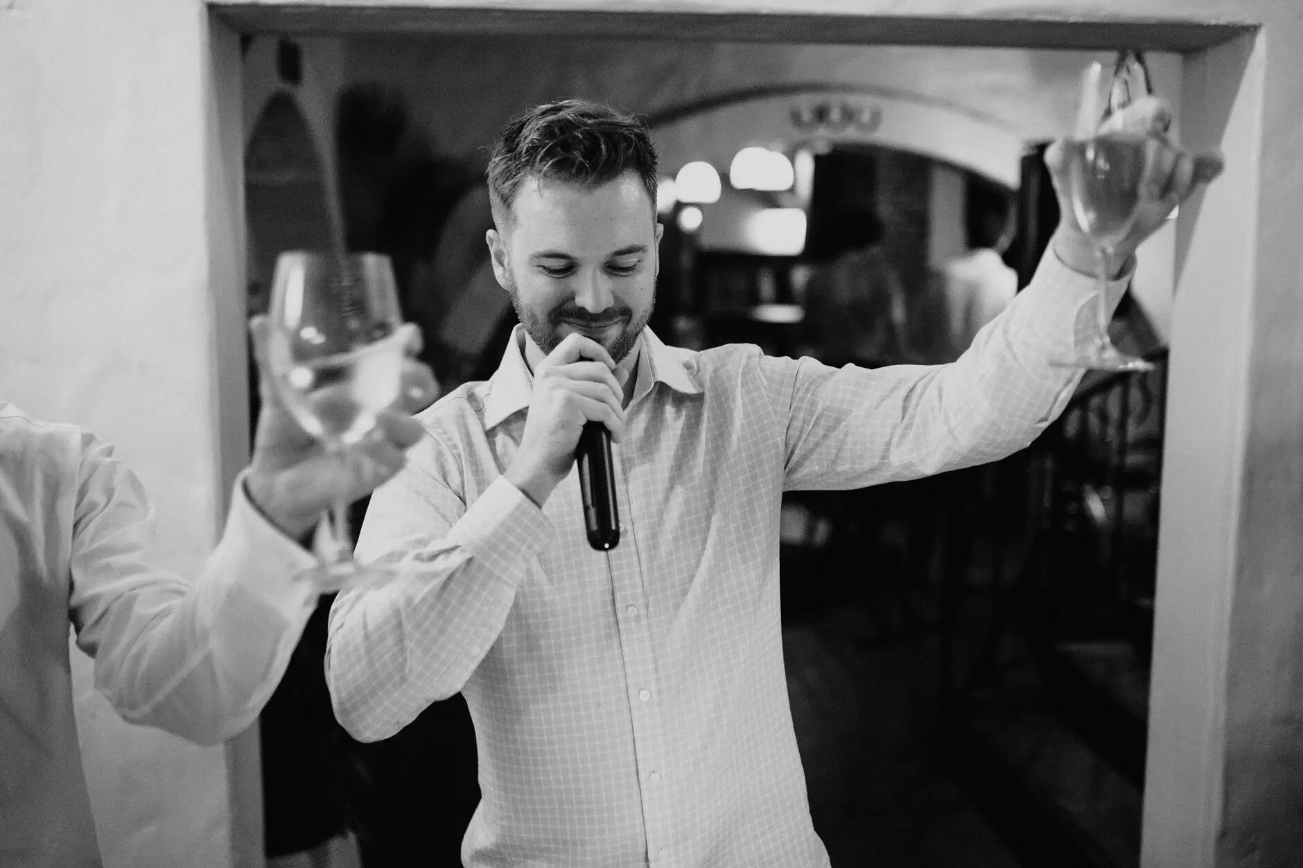 A guest singing into the microphone with his glass raised, in black and white, Porteño, Surry Hills