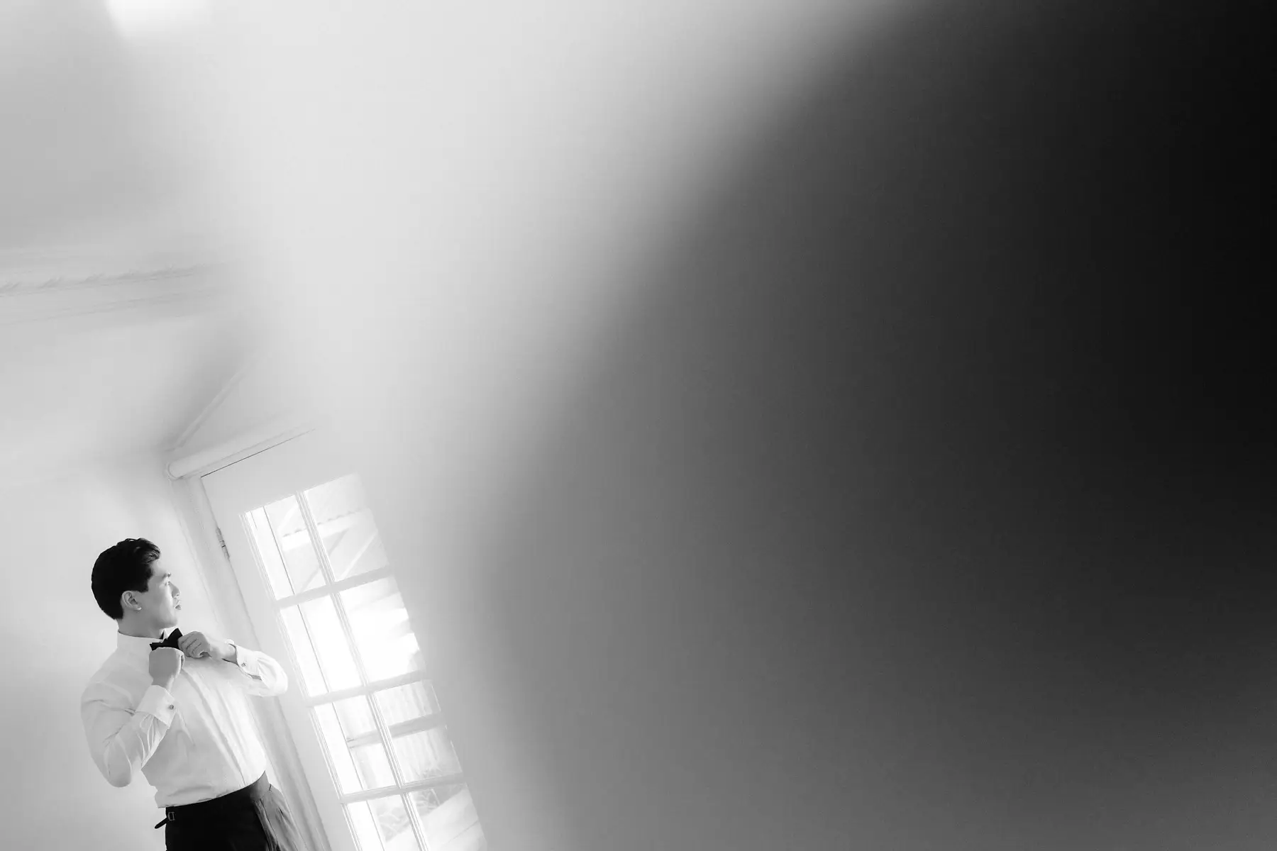 Thomas at the window finishing his bow tie, in black and white, Tall Trees Tallebudgera Valley