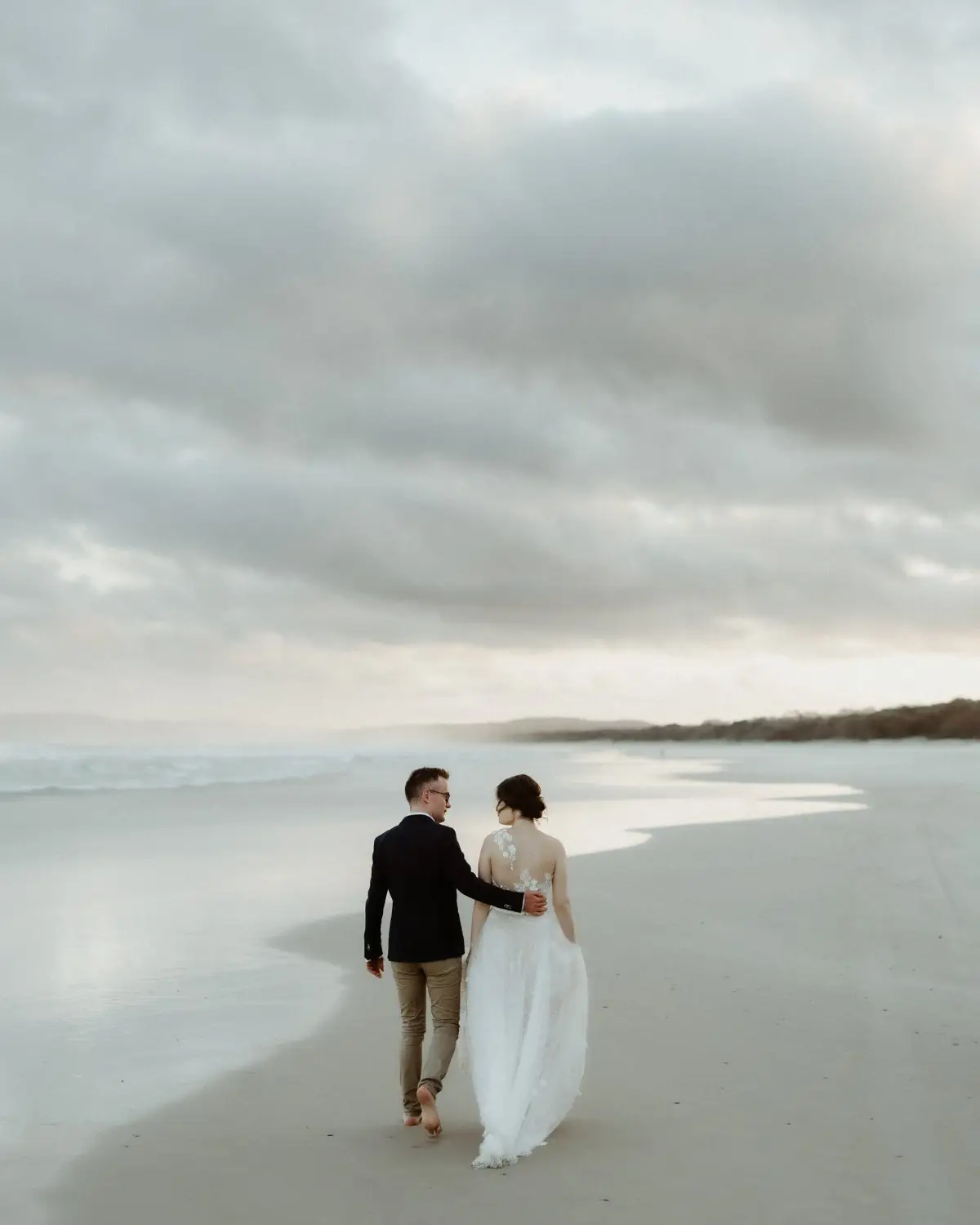 A couple walking barefoot along the wet sand under heavy cloud, Tweed Coast