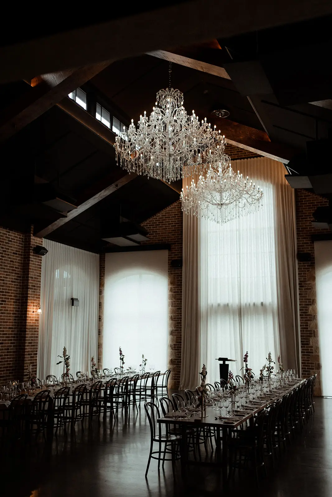 The Manor before guests arrive — chandelier, dark timber trusses and a long table under the drapes, The Valley Estate