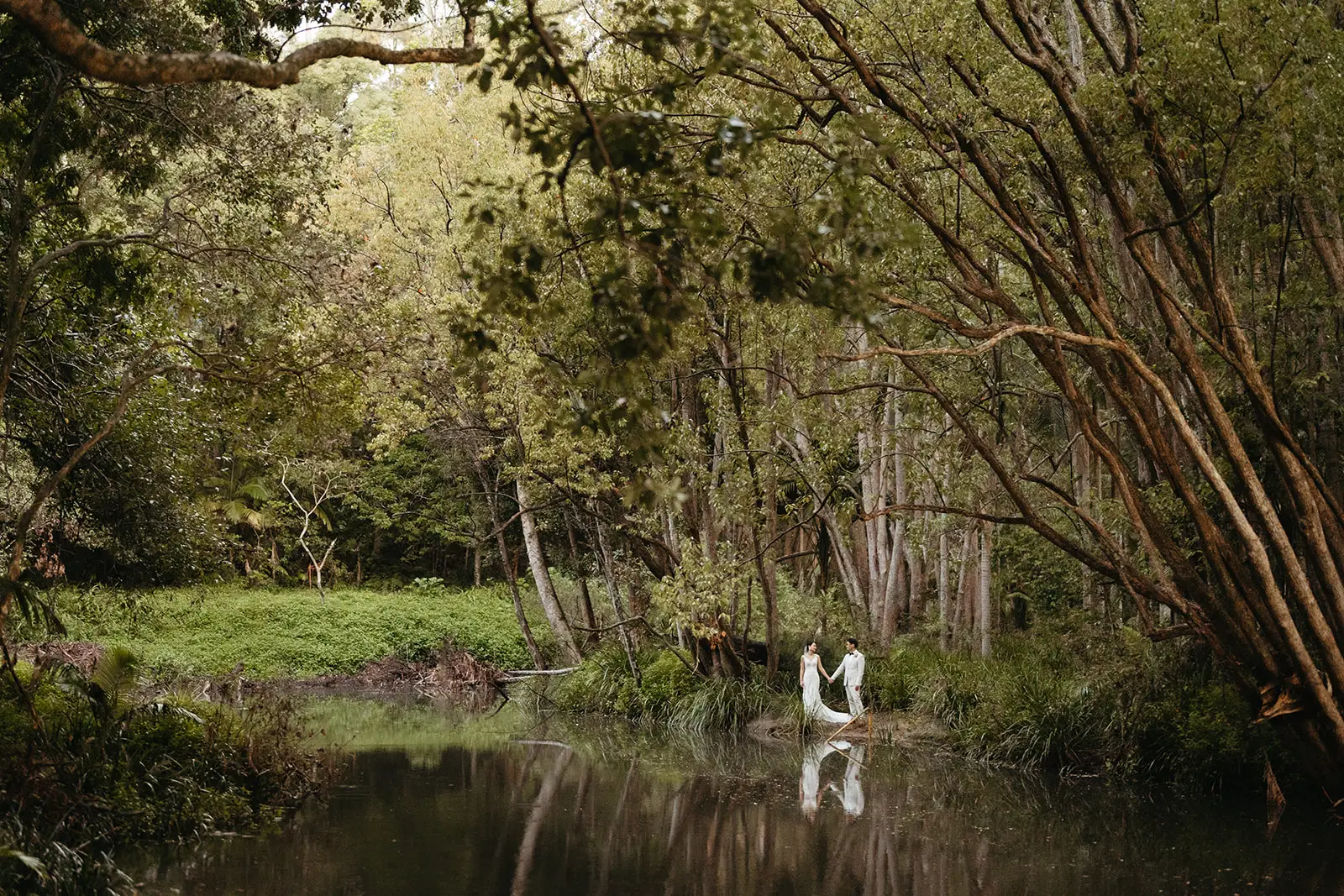 The creek in full frame, the couple small on its bank with their reflection below, The Acre Boomerang Hills