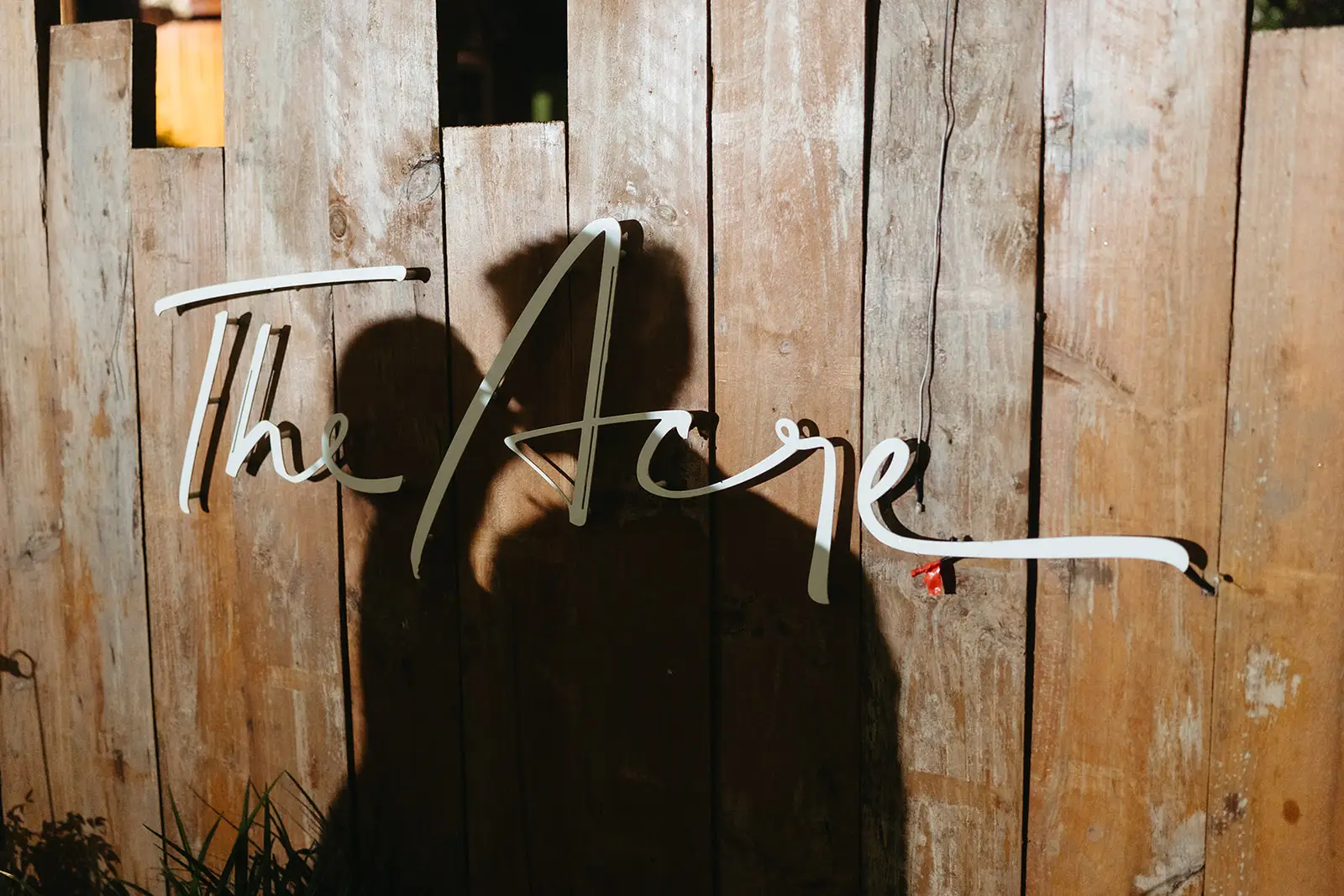 The Acre’s neon sign on the timber fence, the couple’s shadow falling across it