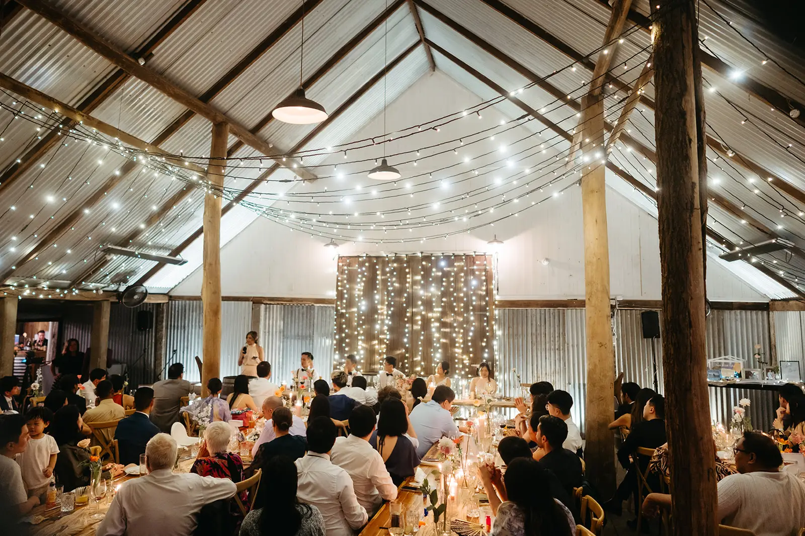Speeches inside the 1902 barn — gabled roof, fairy lights and corrugated iron, The Acre Boomerang Hills